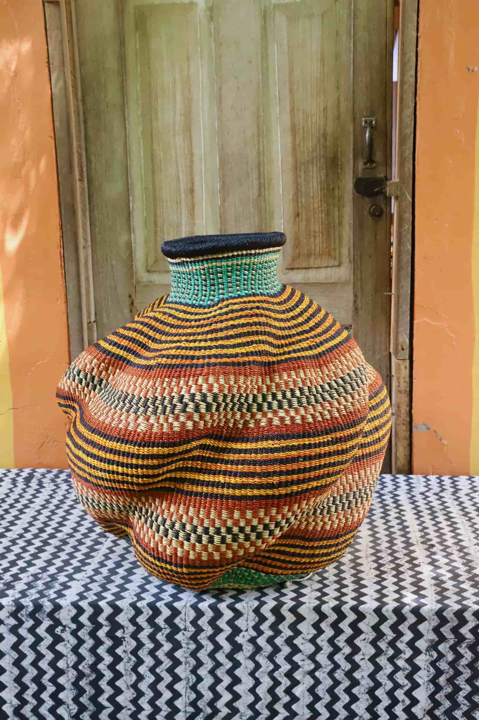 Side view of a handwoven De-engo art basket with a lobed gourd form in amber and black stripes, on a chevron cloth.