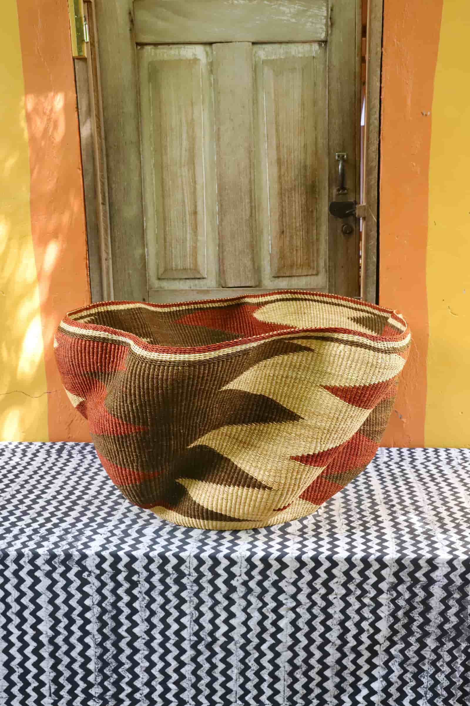 Giant Wave art basket with a dark brown and terracotta wave pattern on a black and white cloth before a wooden door.