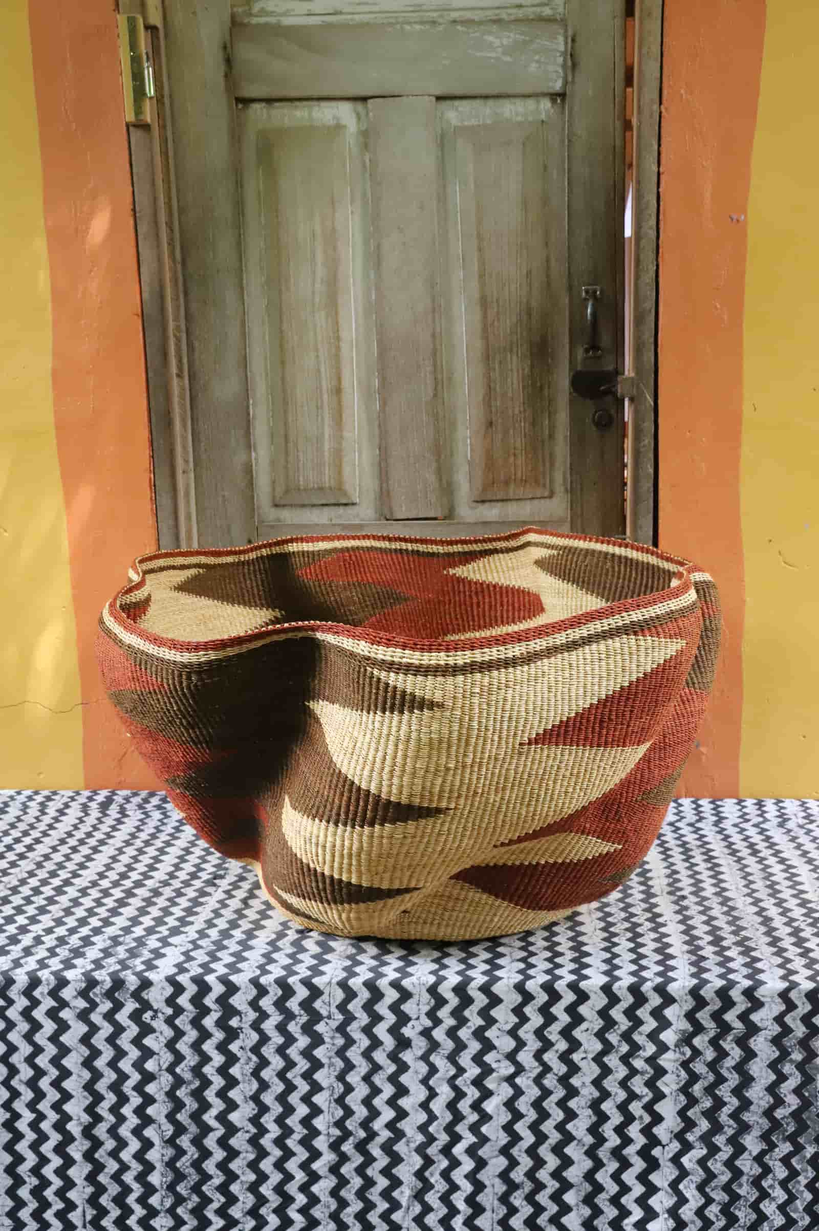 Giant Wave art basket with dark brown and terracotta waves, back view, on a black and white cloth before a wooden door.
