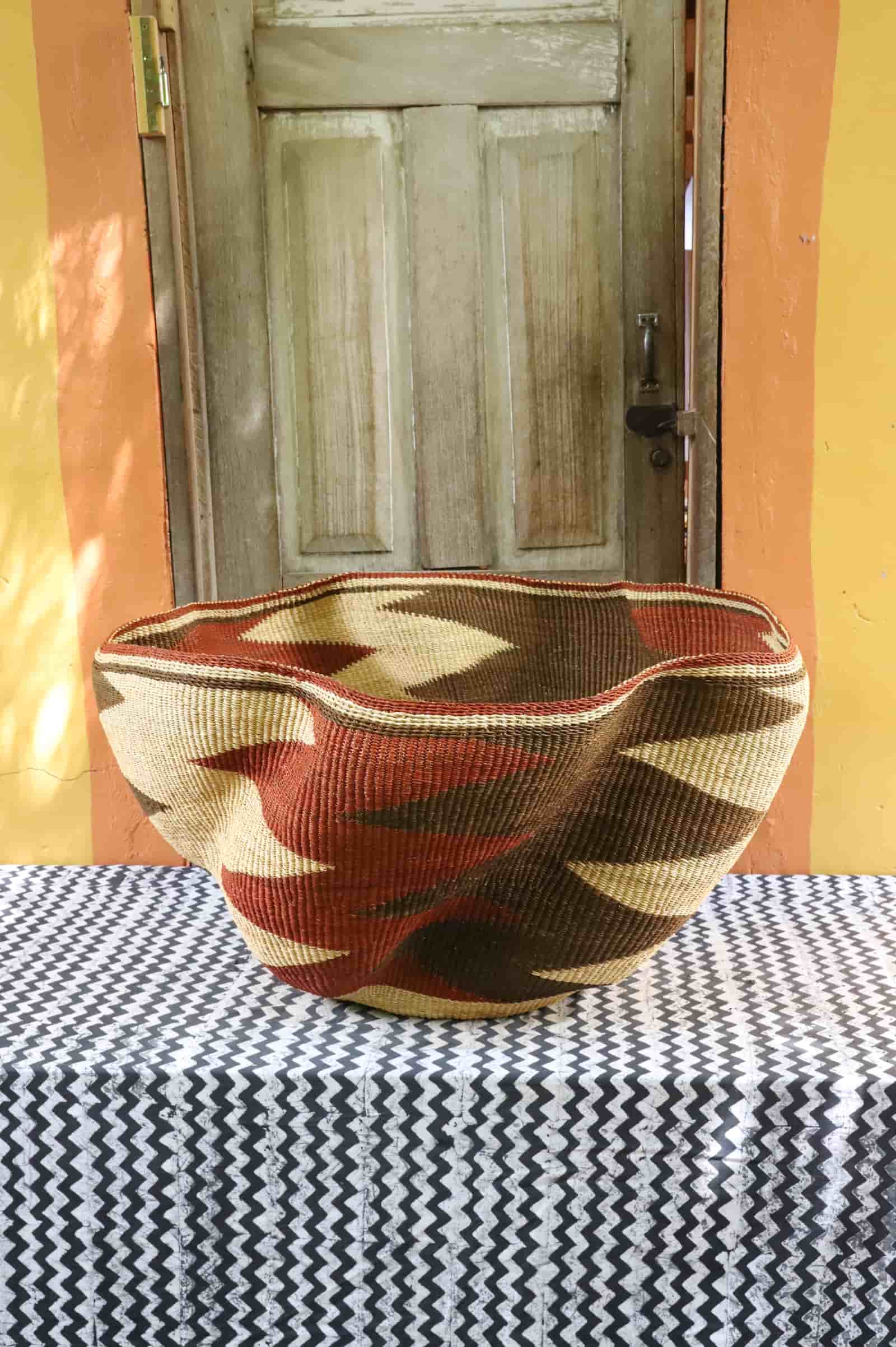 Giant Wave art basket with dark brown and terracotta waves, side view, on a black and white cloth before a wooden door.