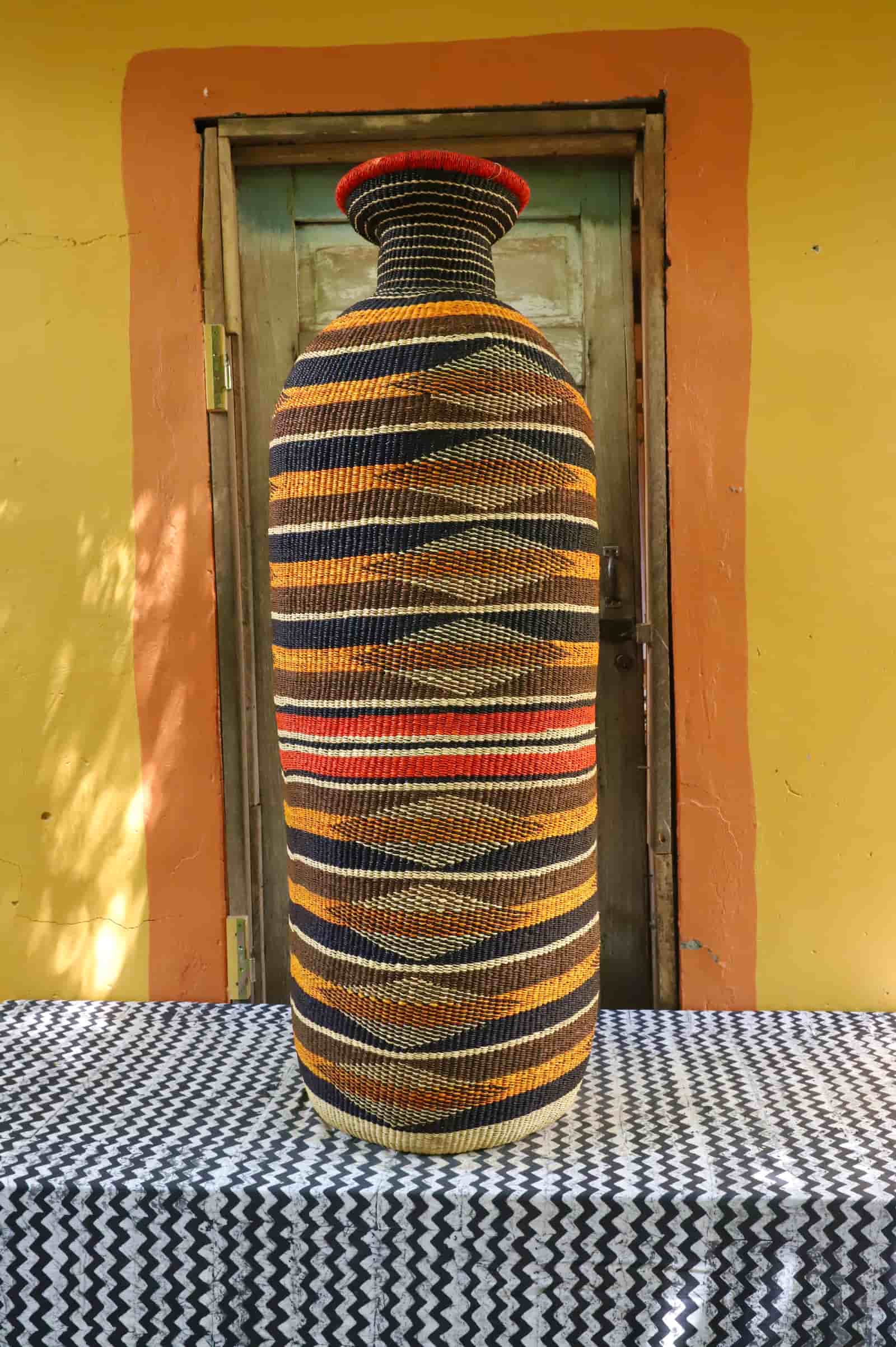 Large Terra Art Basket with vase shape, navy and amber diamond stripe pattern and red accent neck, on chevron cloth