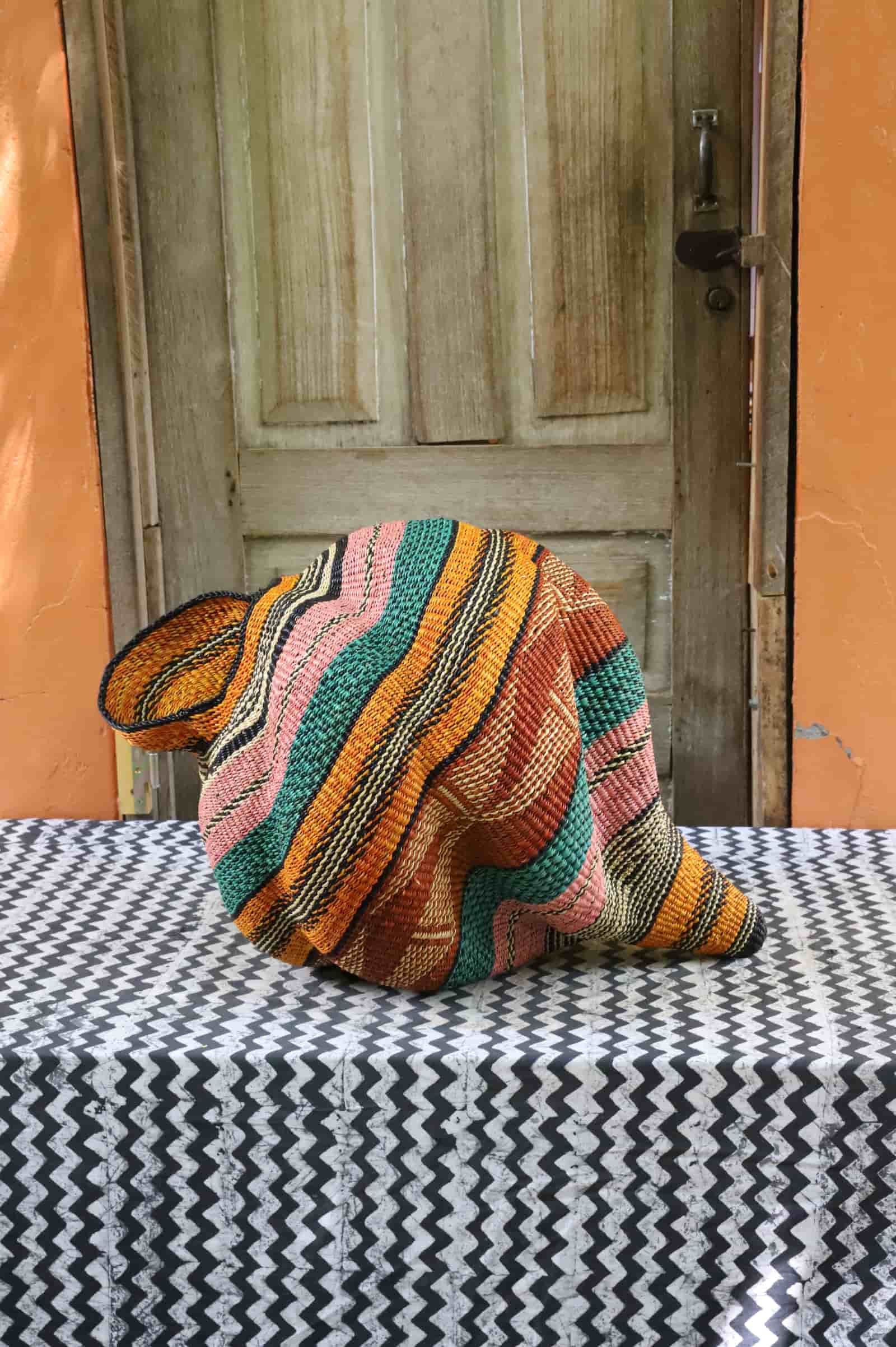 Handwoven Katayeli-tia art basket with teal, amber and pink flowing stripes, on a black and white chevron cloth.