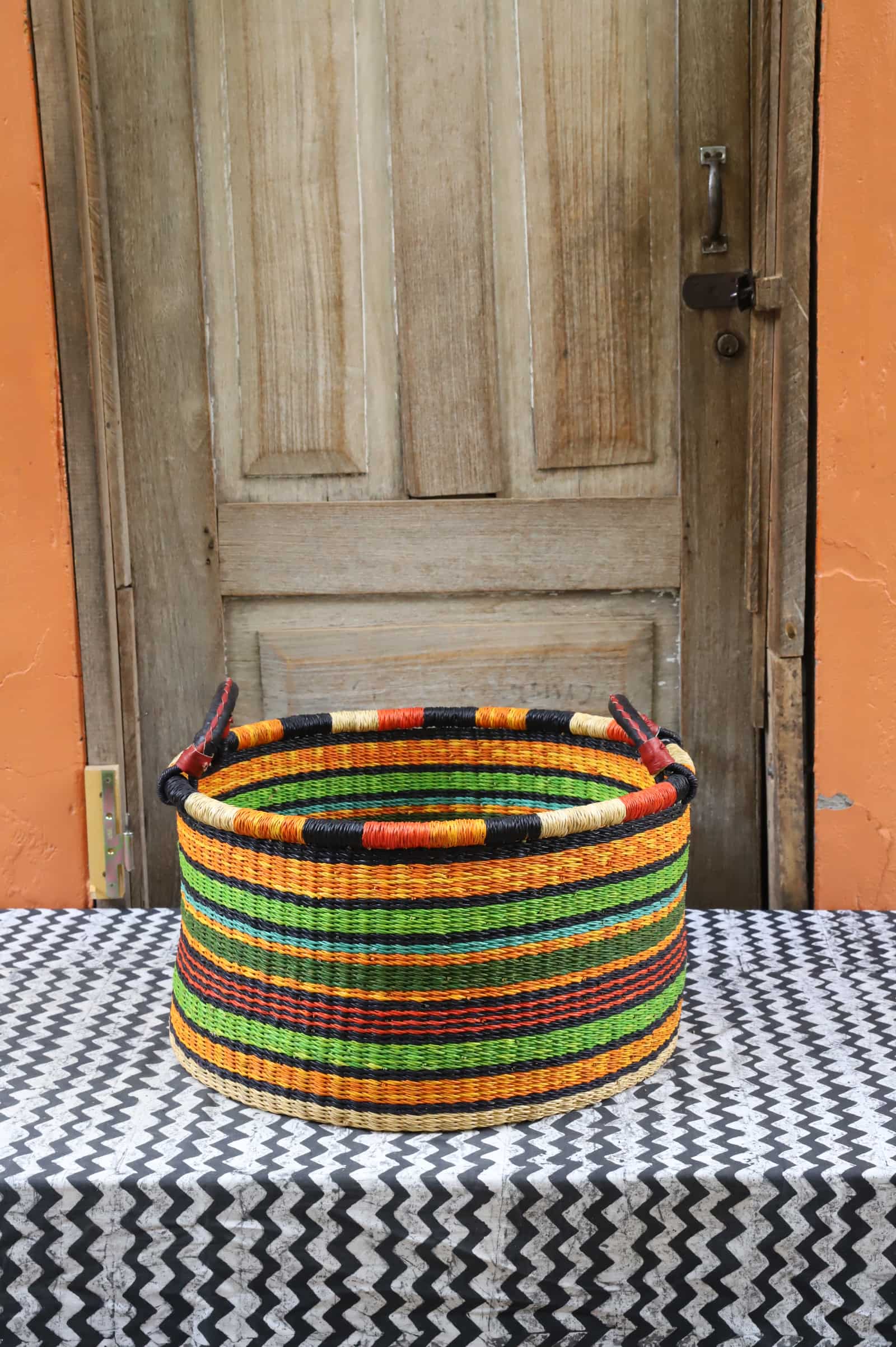 Woven Tub (Medium) handwoven in Ghana sitting on black and white cloth with wooden door background

