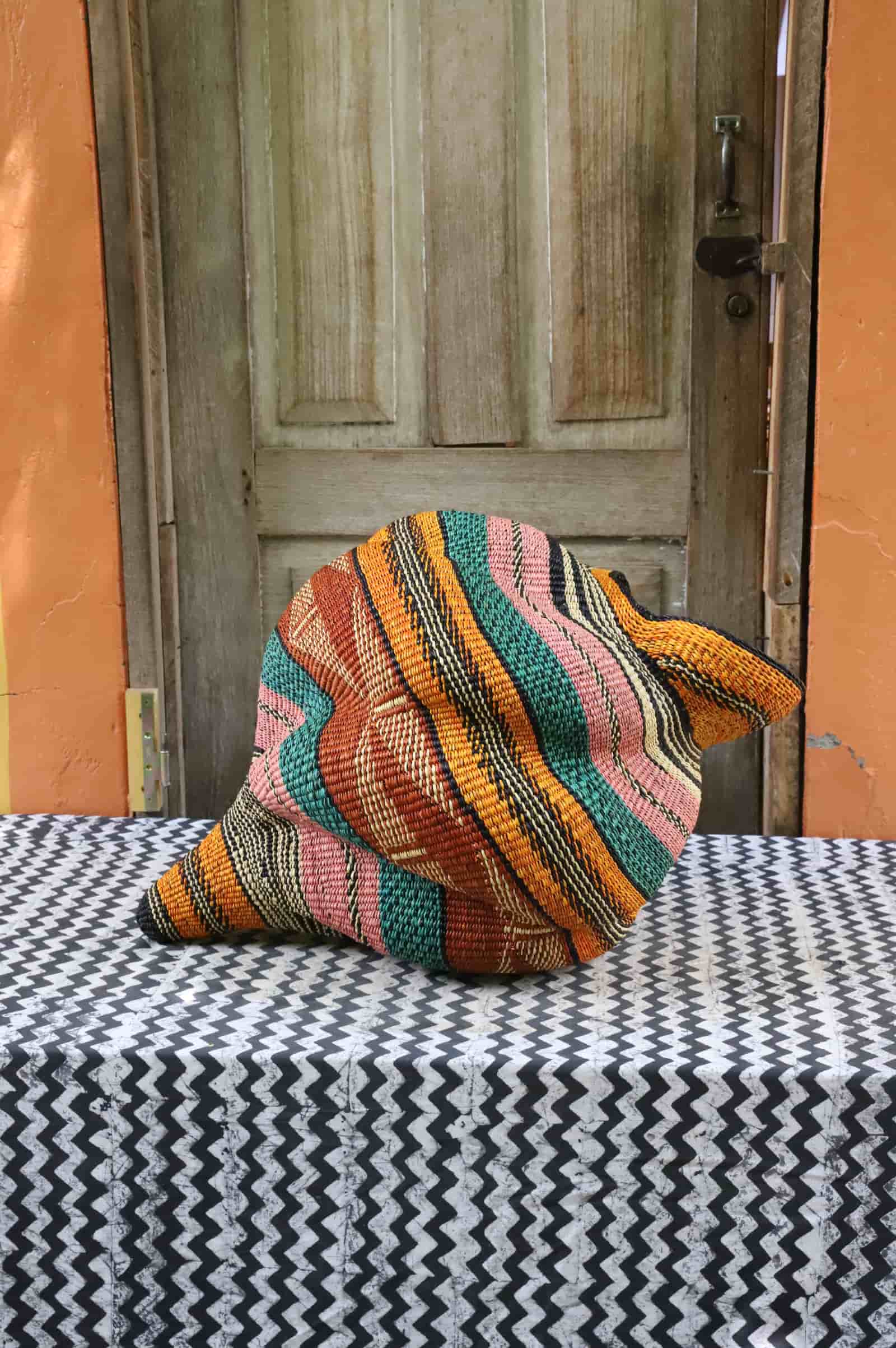 Handwoven Katayeli-tia art basket with teal, terracotta and amber flowing stripes, on a black and white chevron cloth.