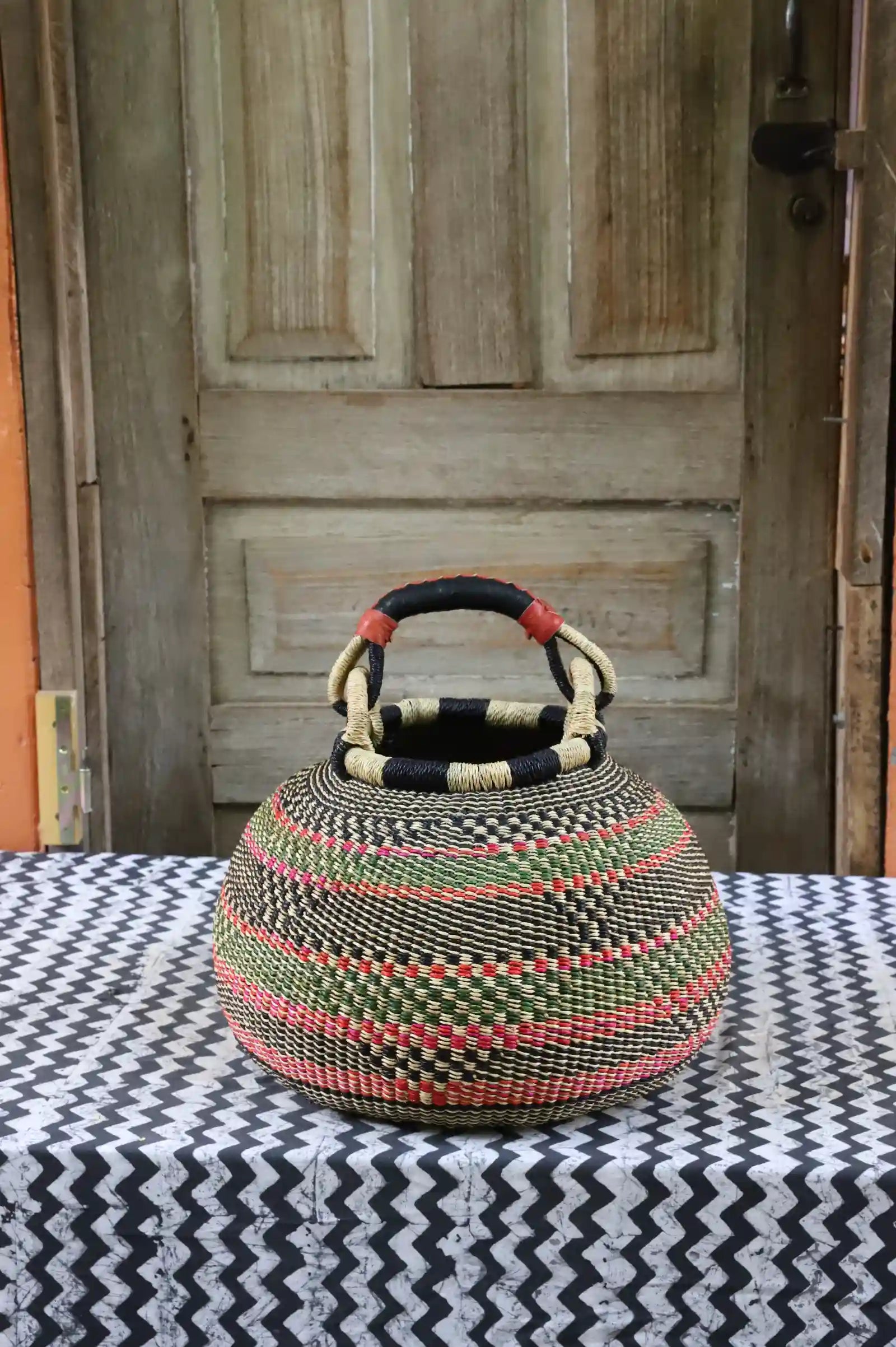 Large pot storage basket in natural straw with green, black and coral woven diagonal stripes