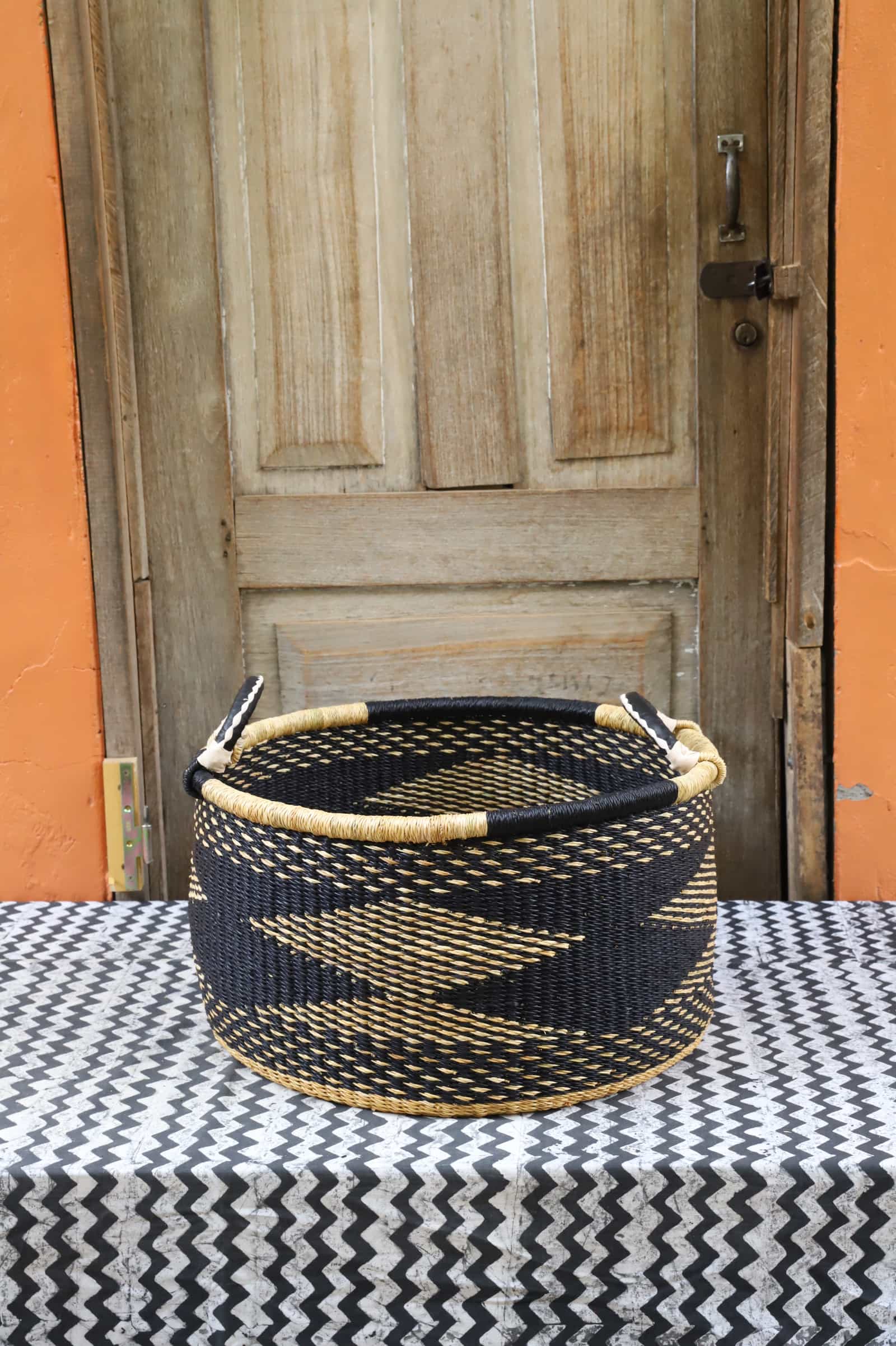 Woven Tub (Small) handwoven in Ghana sitting on black and white cloth with wooden door background

