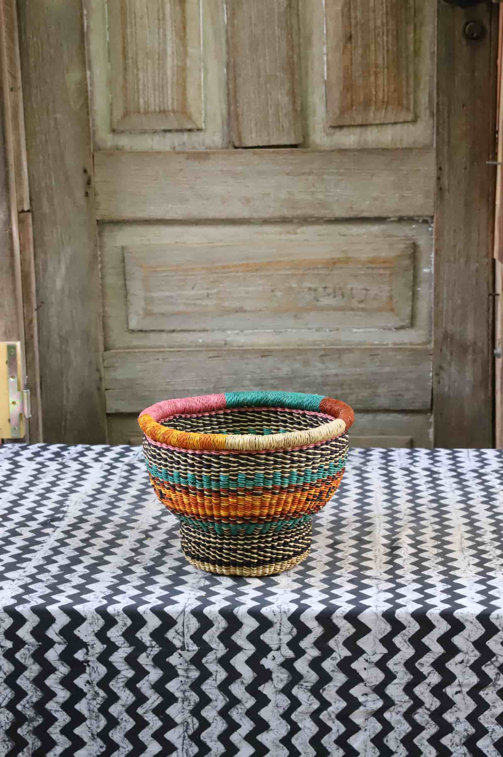 Tiny handwoven drum storage basket with teal, amber and dark red stripes, on a black and white chevron cloth.