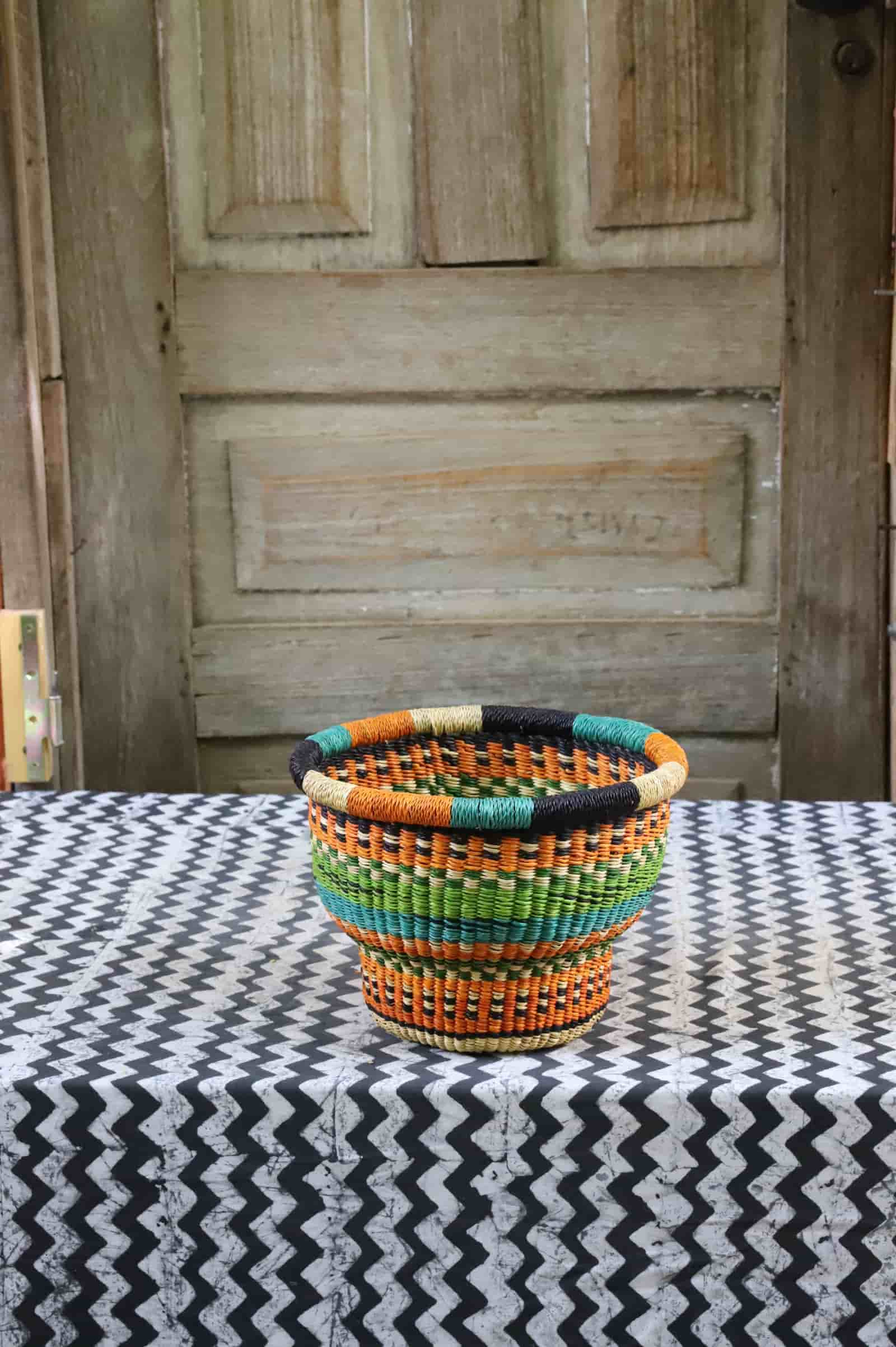 Tiny handwoven drum storage basket with black, teal, lime and orange stripes, on a black and white chevron cloth.