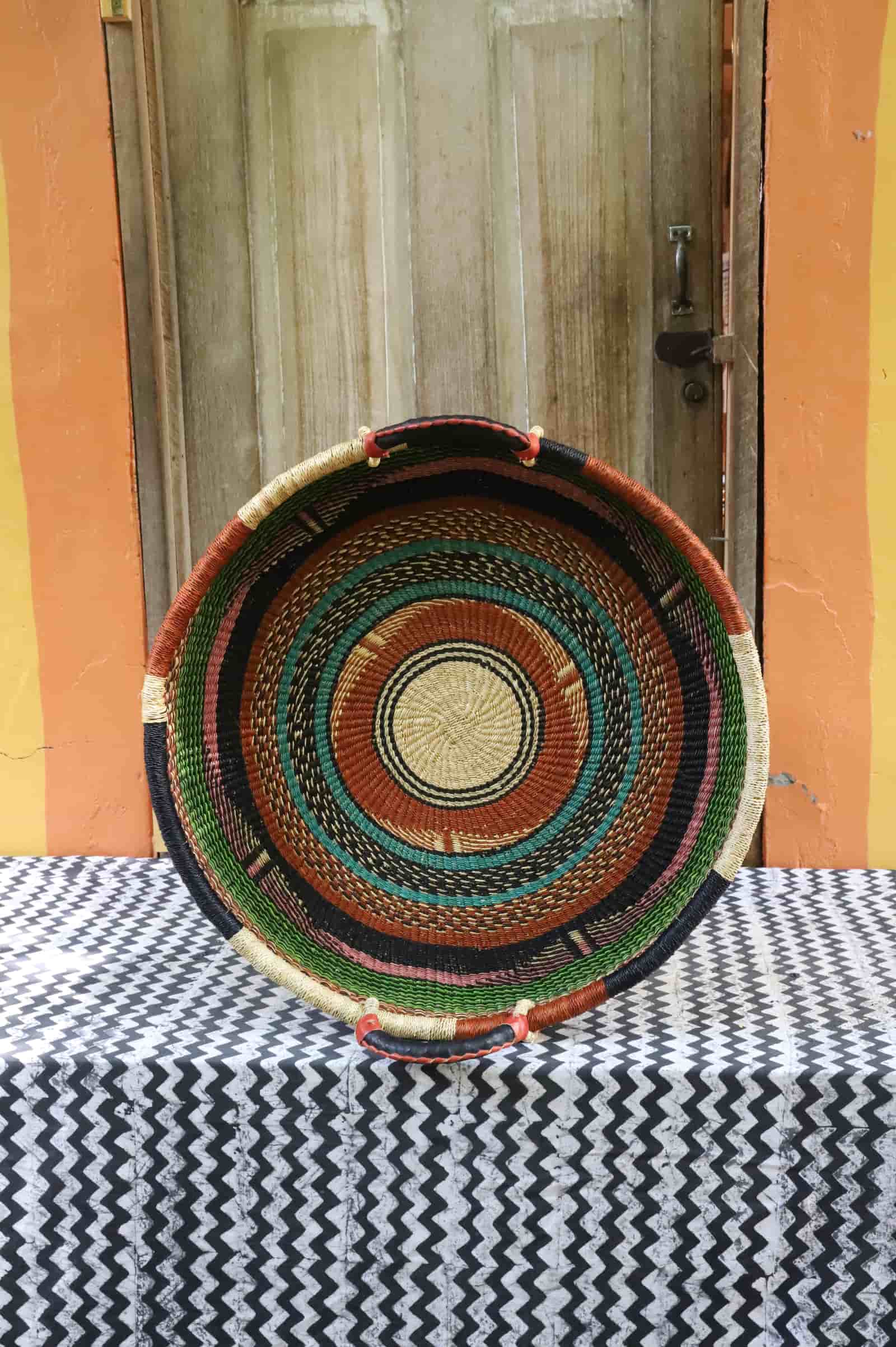Medium double weave woven tray wall décor with concentric rings in dark, terracotta and teal on chevron cloth.