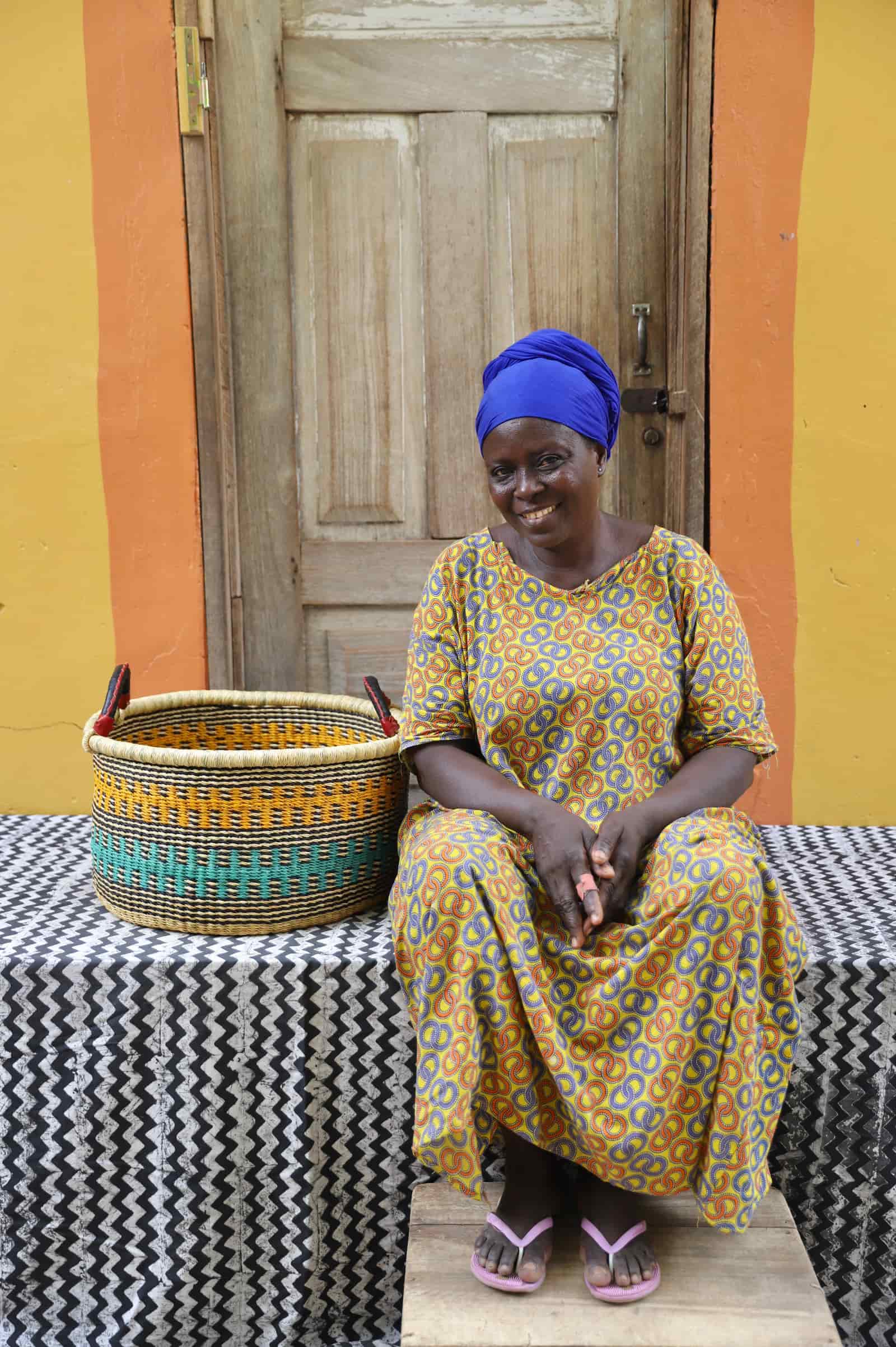 Woven Tub (Small) with woman weaver handwoven in Ghana sitting on black and white cloth and wooden door in background