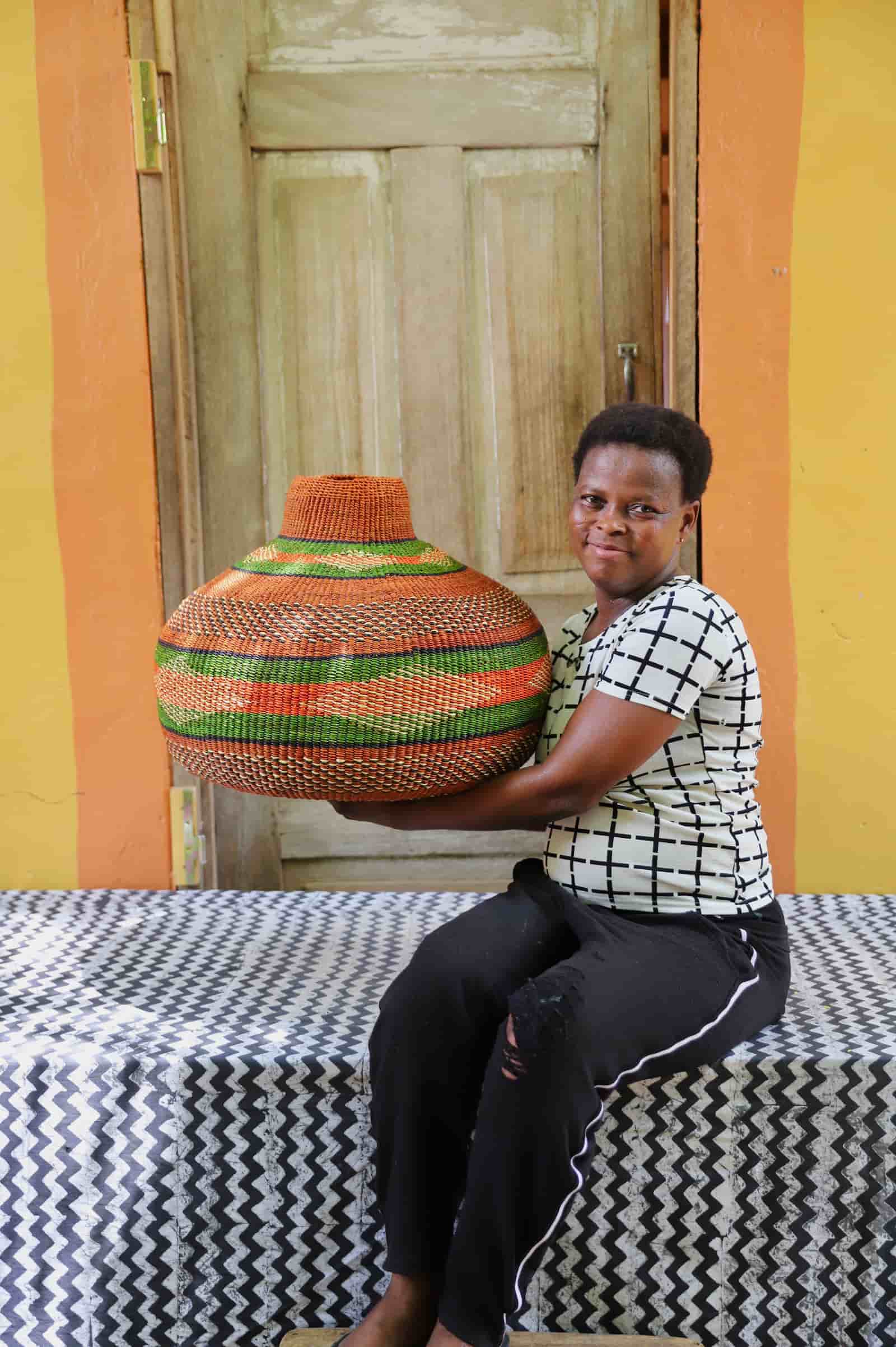 Woman holding Nosere-Yure art basket in rust and green stripes, showing large scale