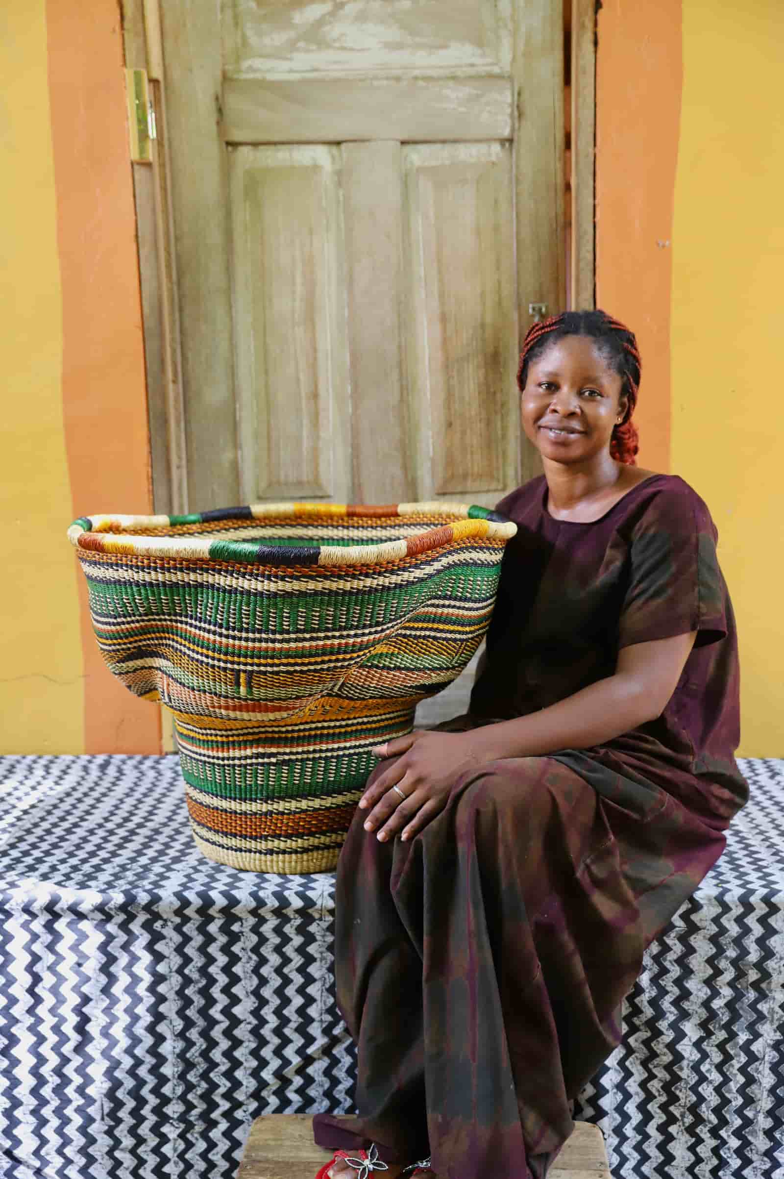 Woman in a dark dress sitting beside a Wave Planter in green and terracotta wave stripe pattern against an orange wall.