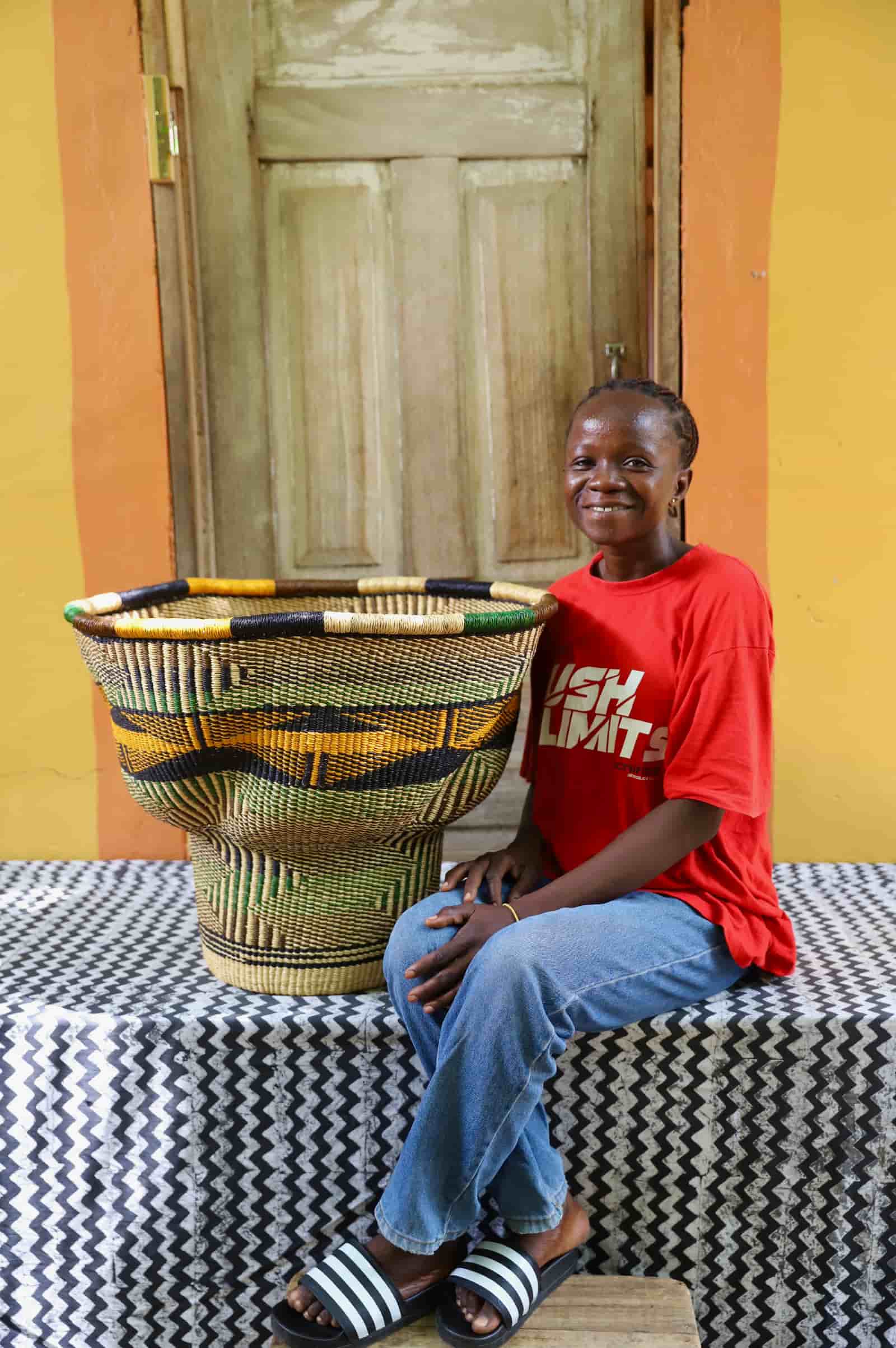 Woman in a red t-shirt sitting beside a Wave Planter in green, black and yellow stripe pattern against an orange wall.