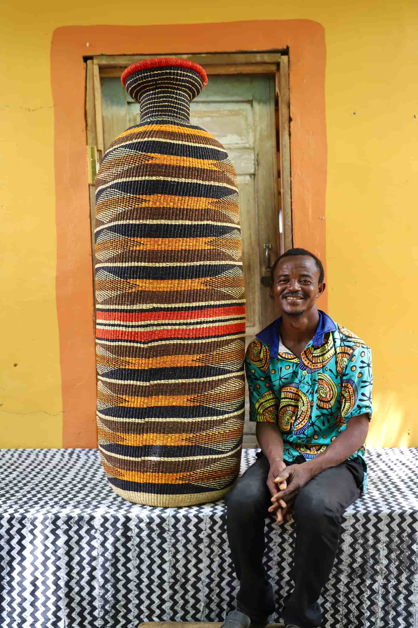 Man seated beside a floor-height large Terra Art Basket with navy and amber horizontal stripe pattern