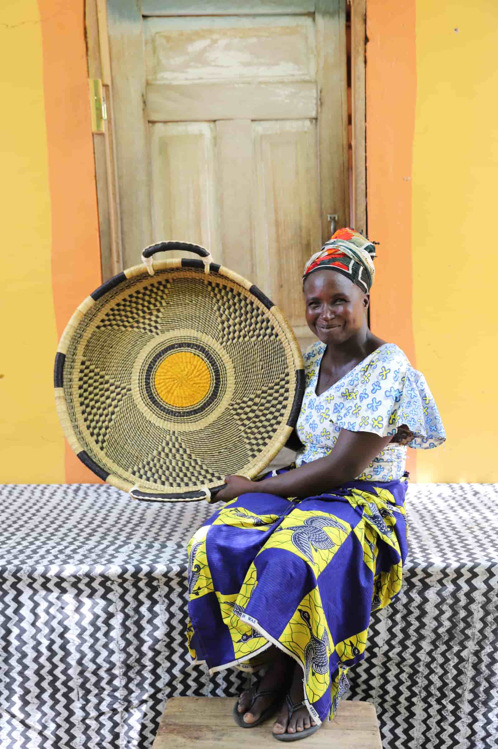 Woman in a blue and yellow dress holding a medium double weave woven tray in black and natural geometric checker pattern.