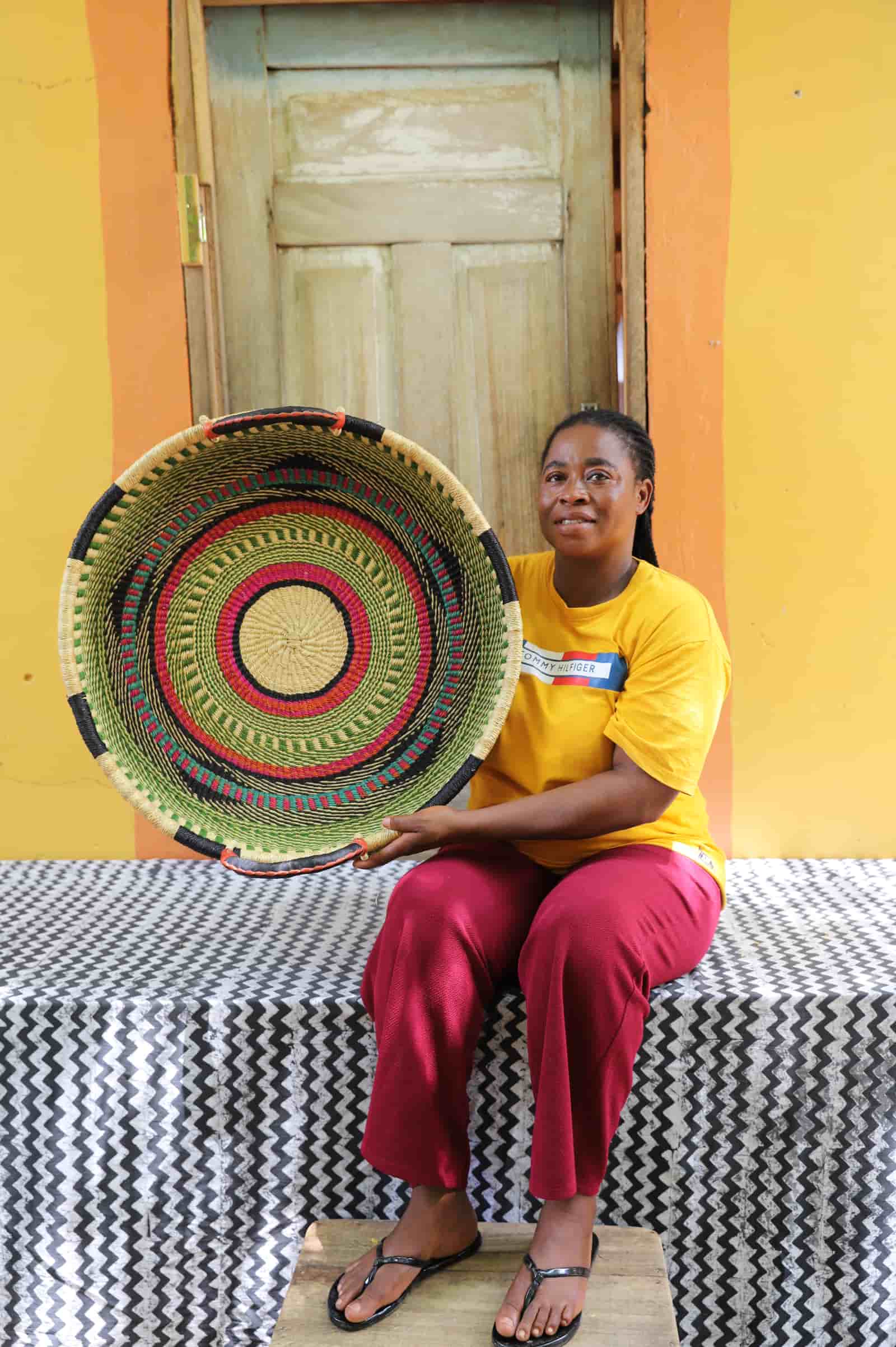 Woman in a yellow top holding a medium double weave woven tray in green, magenta and black concentric ring pattern.