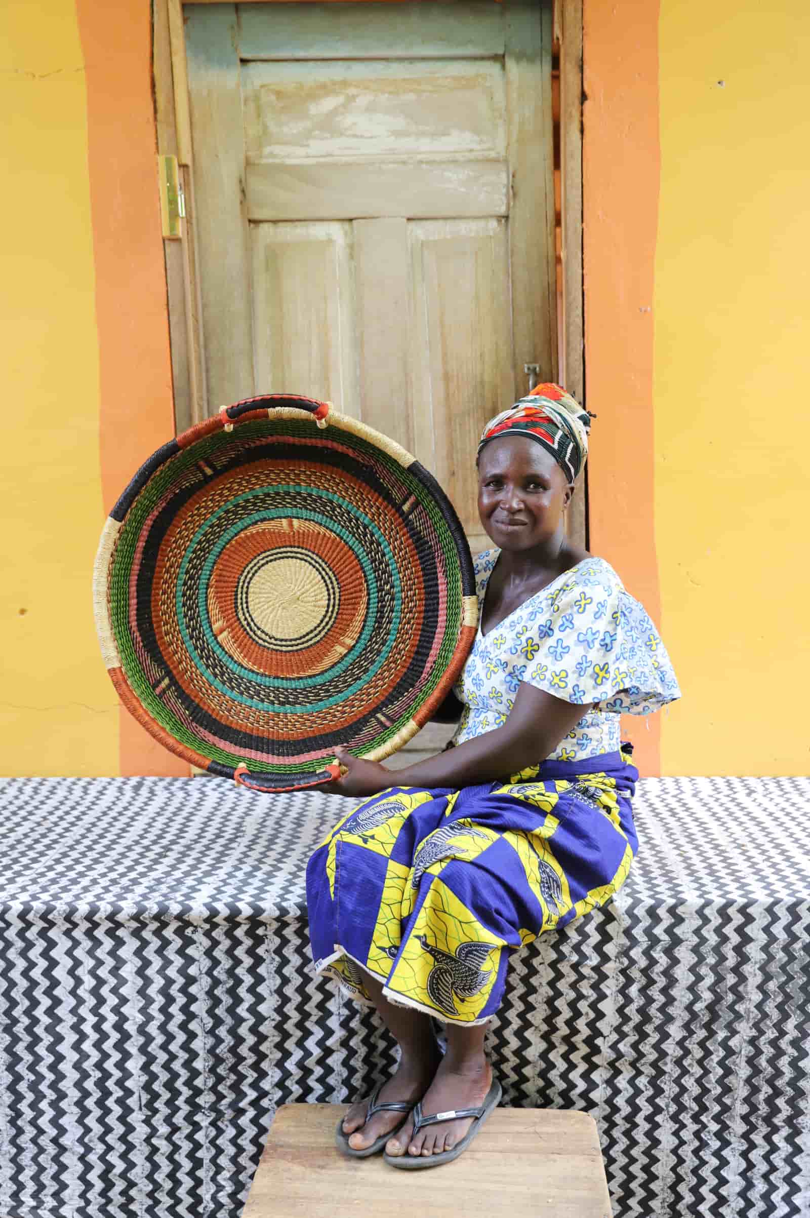 Woman in a patterned dress holding a medium double weave woven tray in dark, teal and orange concentric ring pattern.