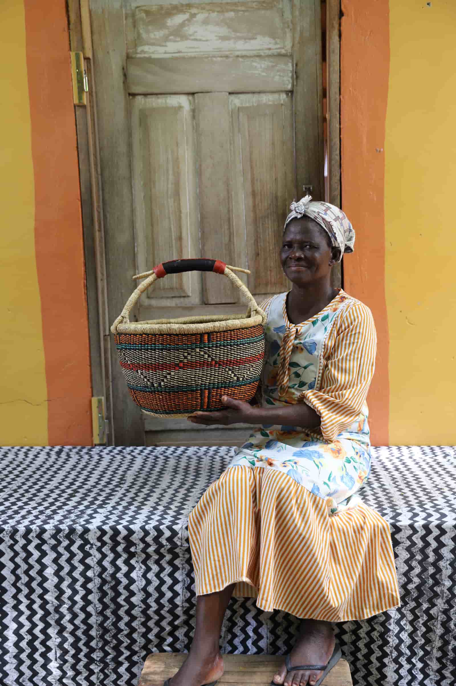 Woman in yellow striped dress holding a large teal and terracotta patterned Bolga shopping basket