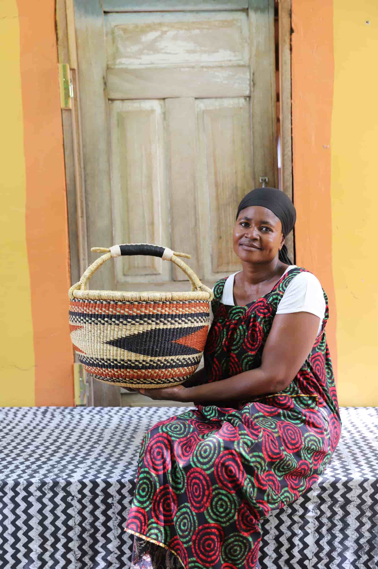Woman in dark floral African print dress holding a large black and natural patterned Bolga shopping basket