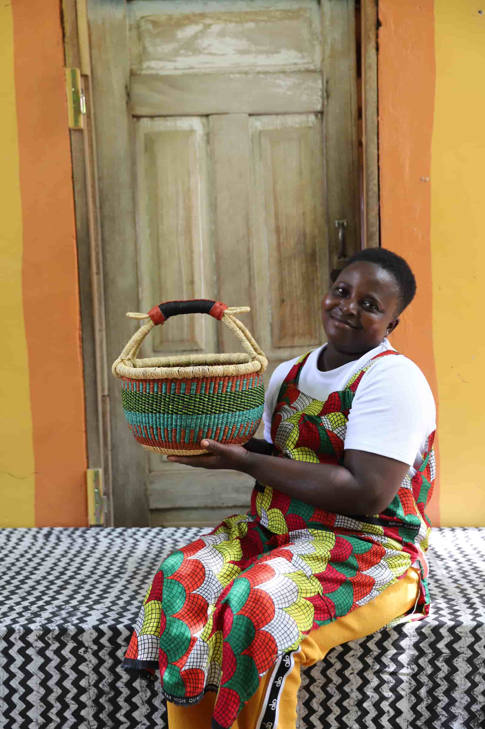Woman in colourful African print dress holding a small green and teal Bolga shopping basket