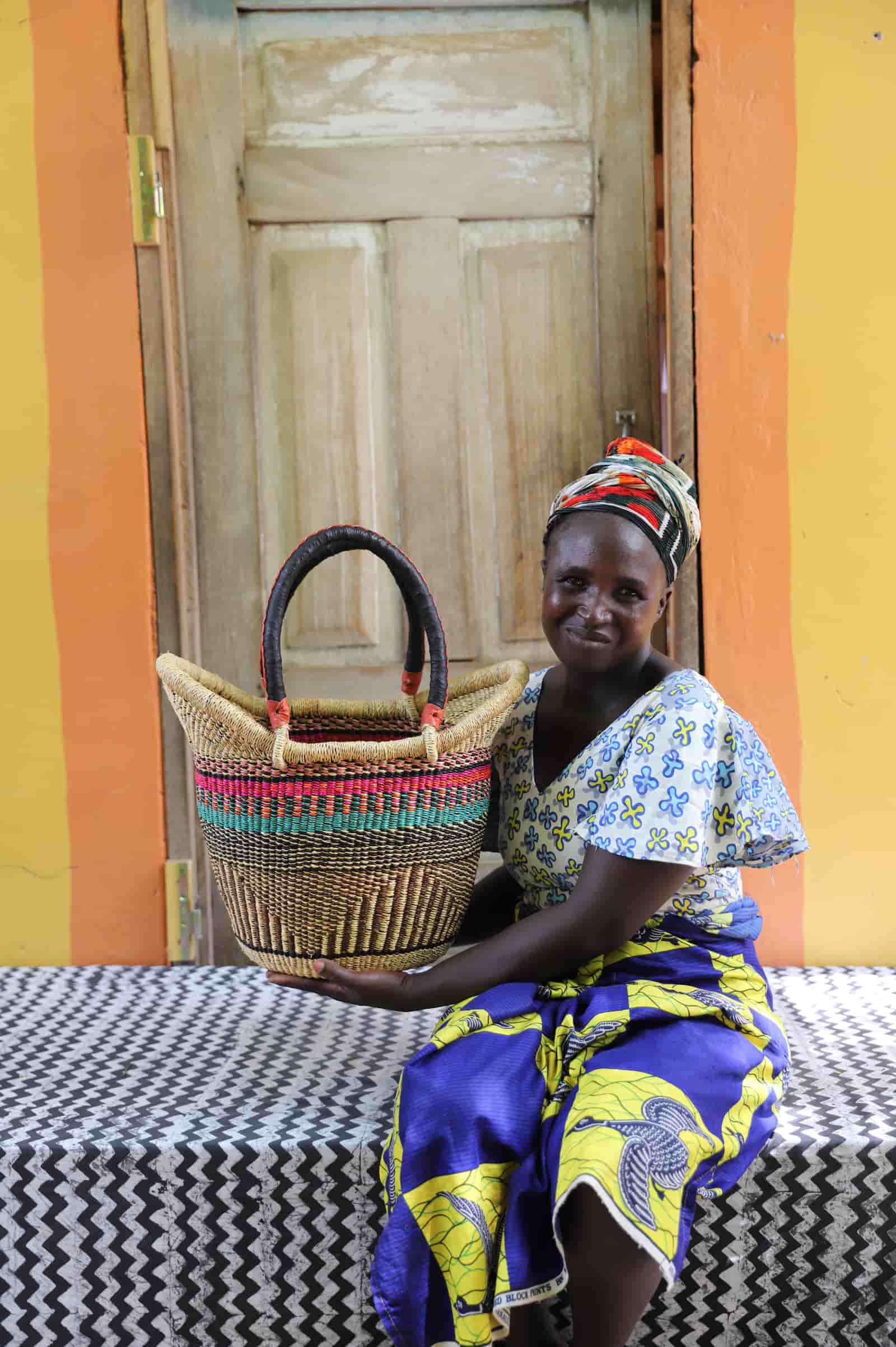 Woman holding Nyariga shopping basket in natural straw with pink and teal stripe detail