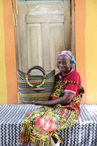 Woman in yellow and red African print dress holding a woven black and natural striped beach bag