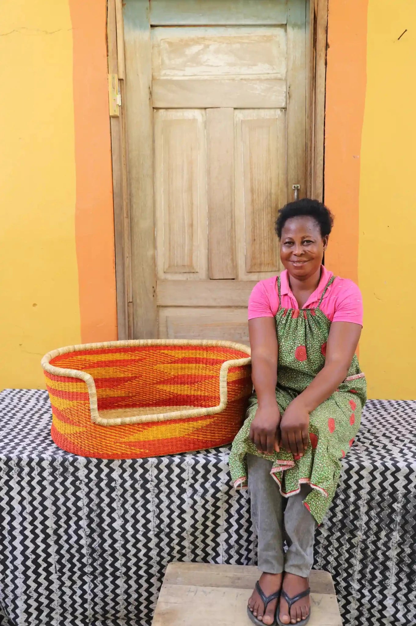 Man  sitting on a bench with a woven basket next to a wooden door and yellow wall.