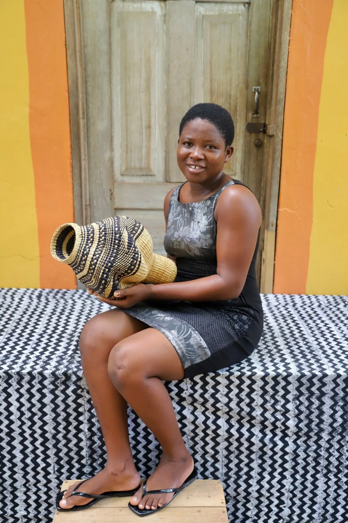Woman holding a woven conch piece on a black and white patterned surface with a wooden door in the background.