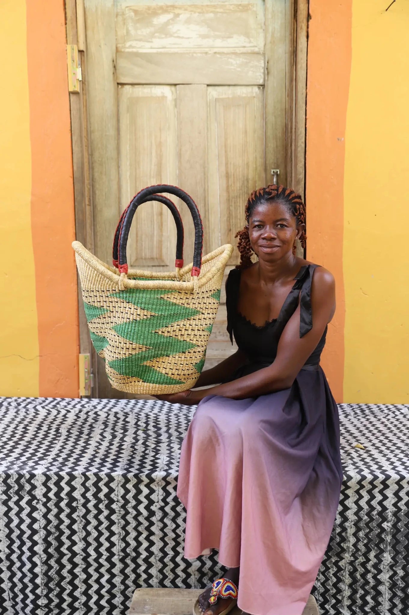 Woman in black top and pink skirt holding a large Solara Carryall with green and natural diamond pattern