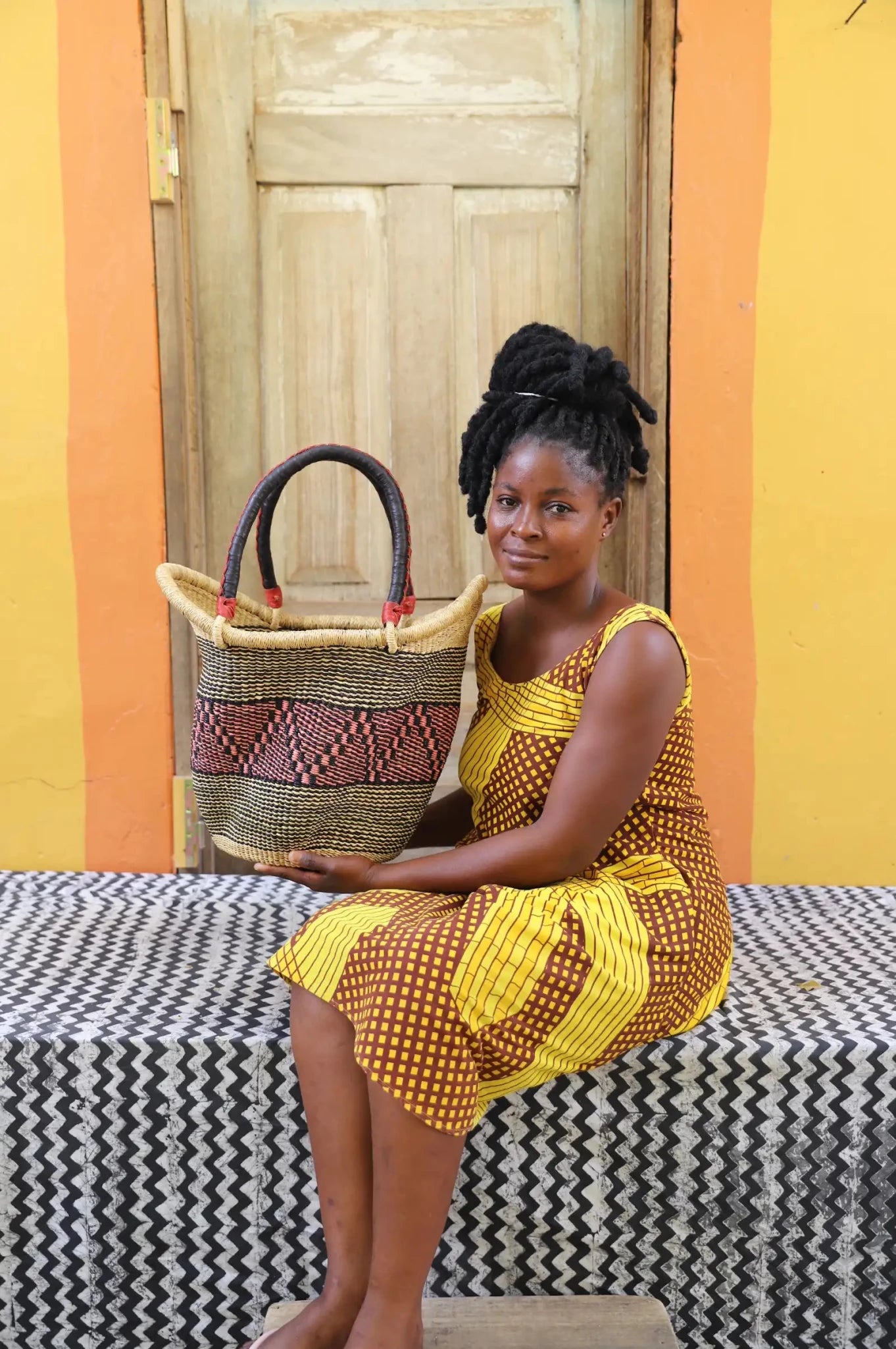 Woman in yellow and brown print dress holding a large Solara Carryall with natural and burgundy woven band