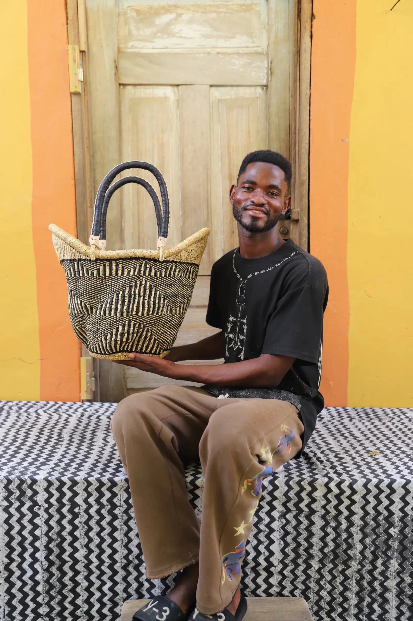 Man in black t-shirt holding a large Solara Carryall with dark and natural check pattern, leather handles