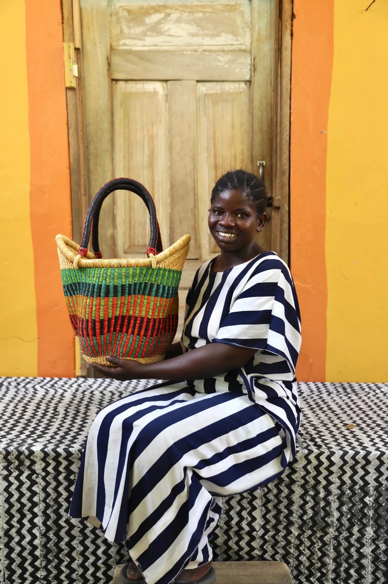 Woman in blue and white striped dress holding a large Solara Carryall with green, red and natural stripe