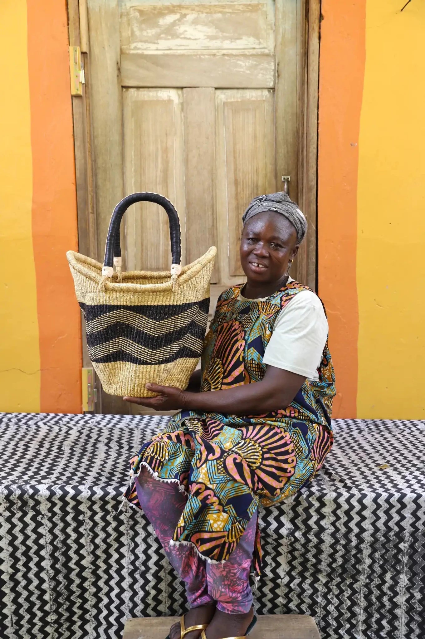 Woman in colourful print dress holding a medium Solara Carryall with natural and black zigzag pattern
