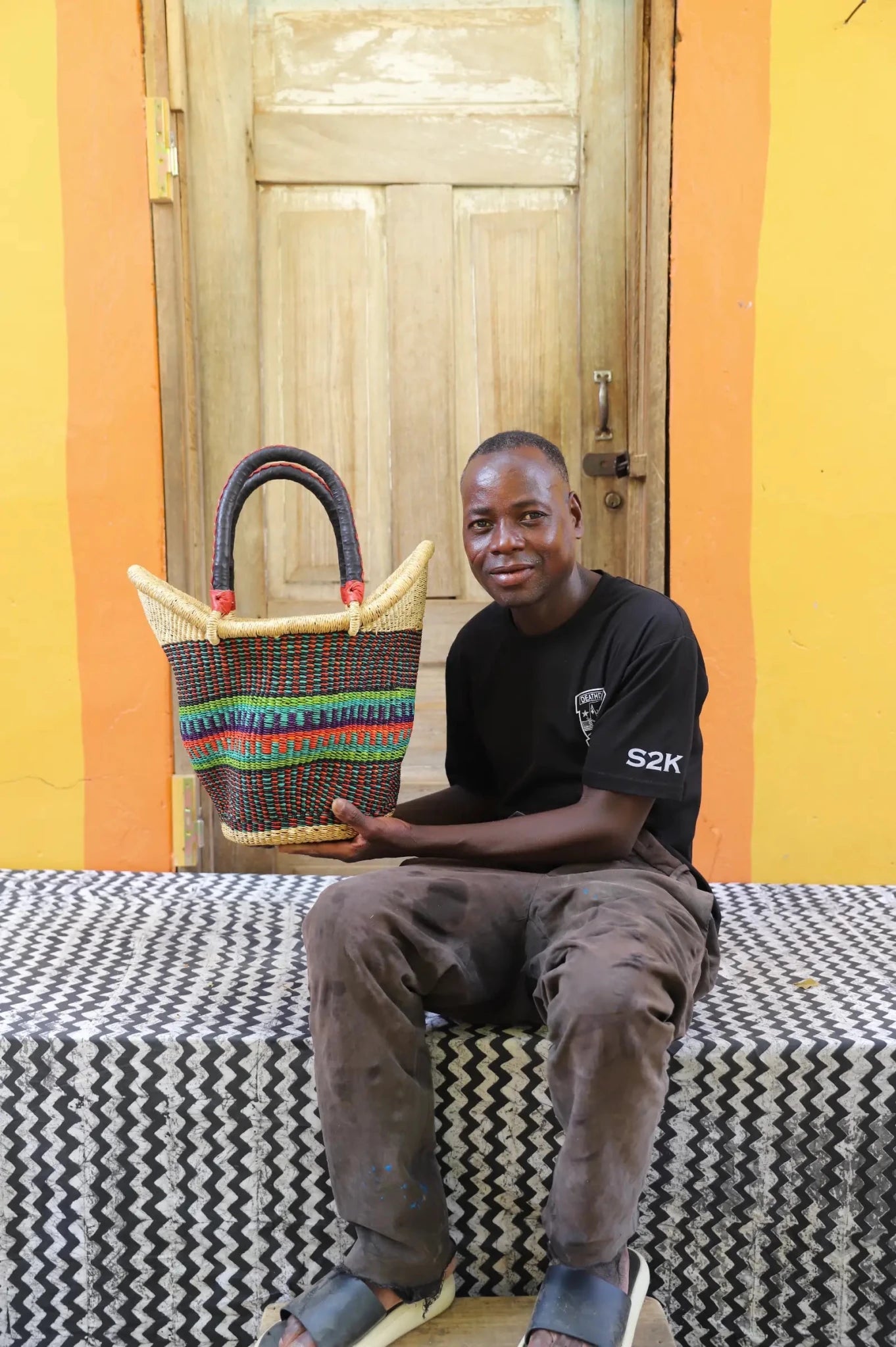 Man in black t-shirt holding a medium dark Solara Carryall with multicolour stripe band and leather handles