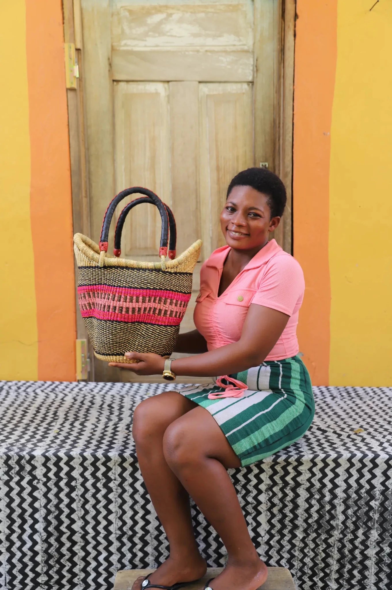 Woman in pink polo shirt holding a small Solara Carryall with natural and pink stripe, dark leather handles
