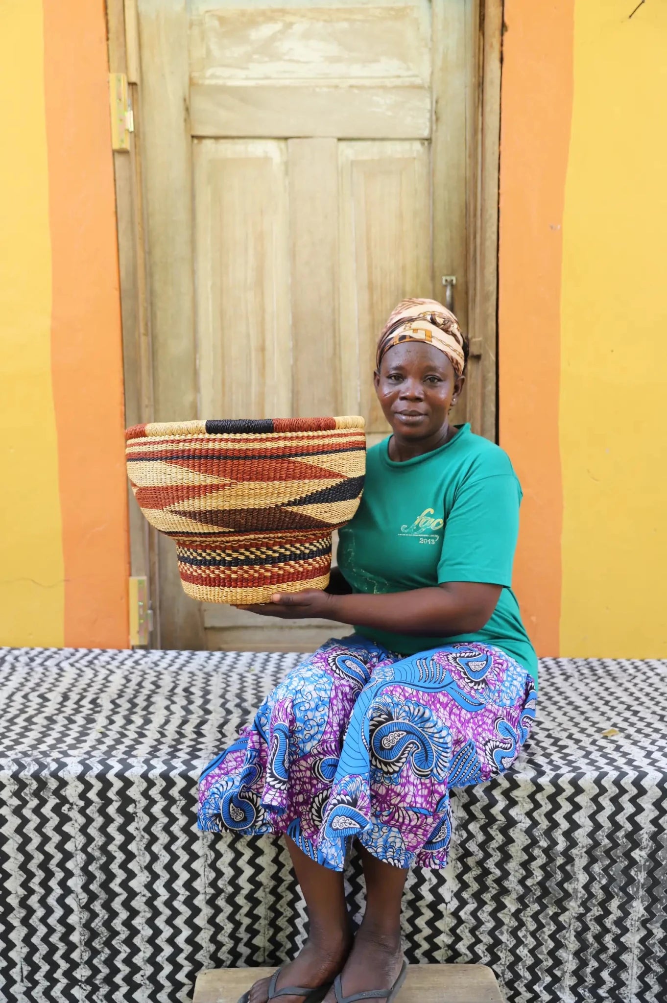 Woman holding a woven basket in front of a colorful wall.