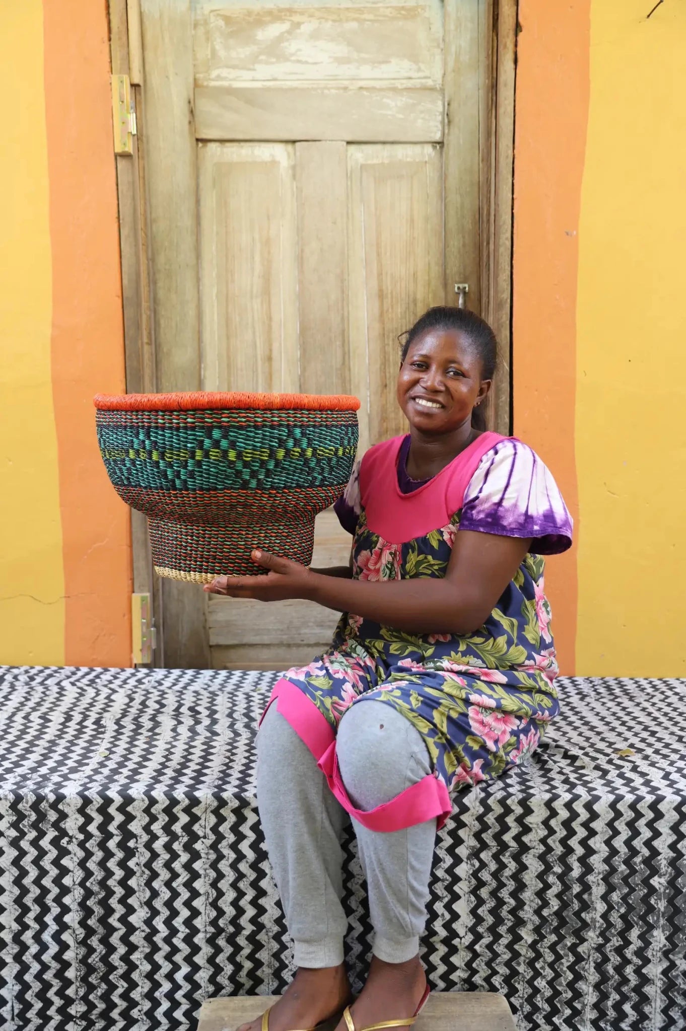 Woman holding a woven basket in front of a colorful wall.