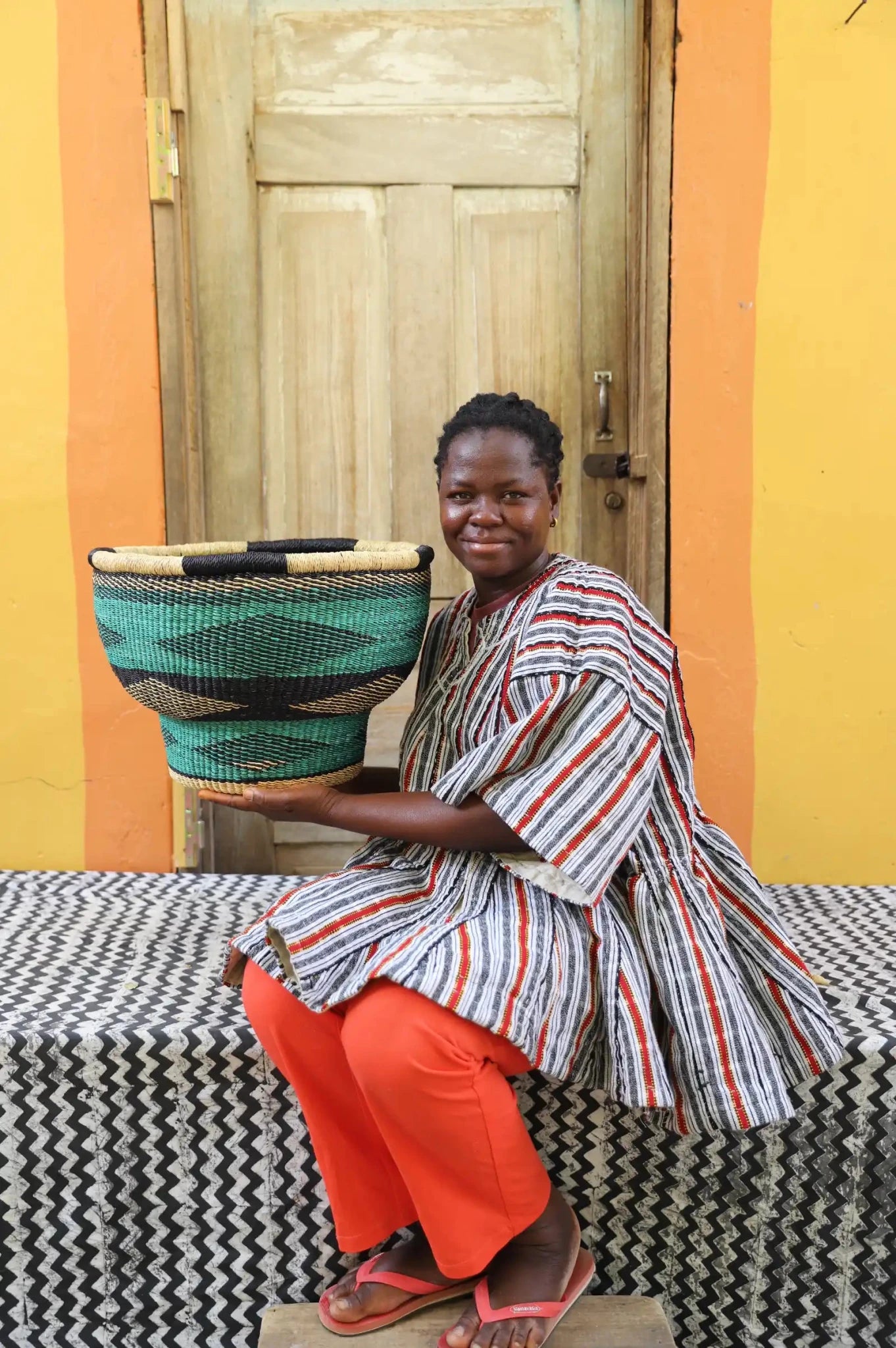 Woman holding a woven basket in front of a colorful wall.