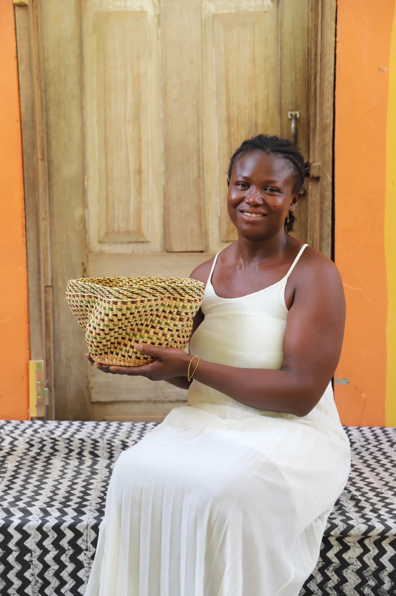 Woman holding a woven basket in front of an orange wall and wooden door.