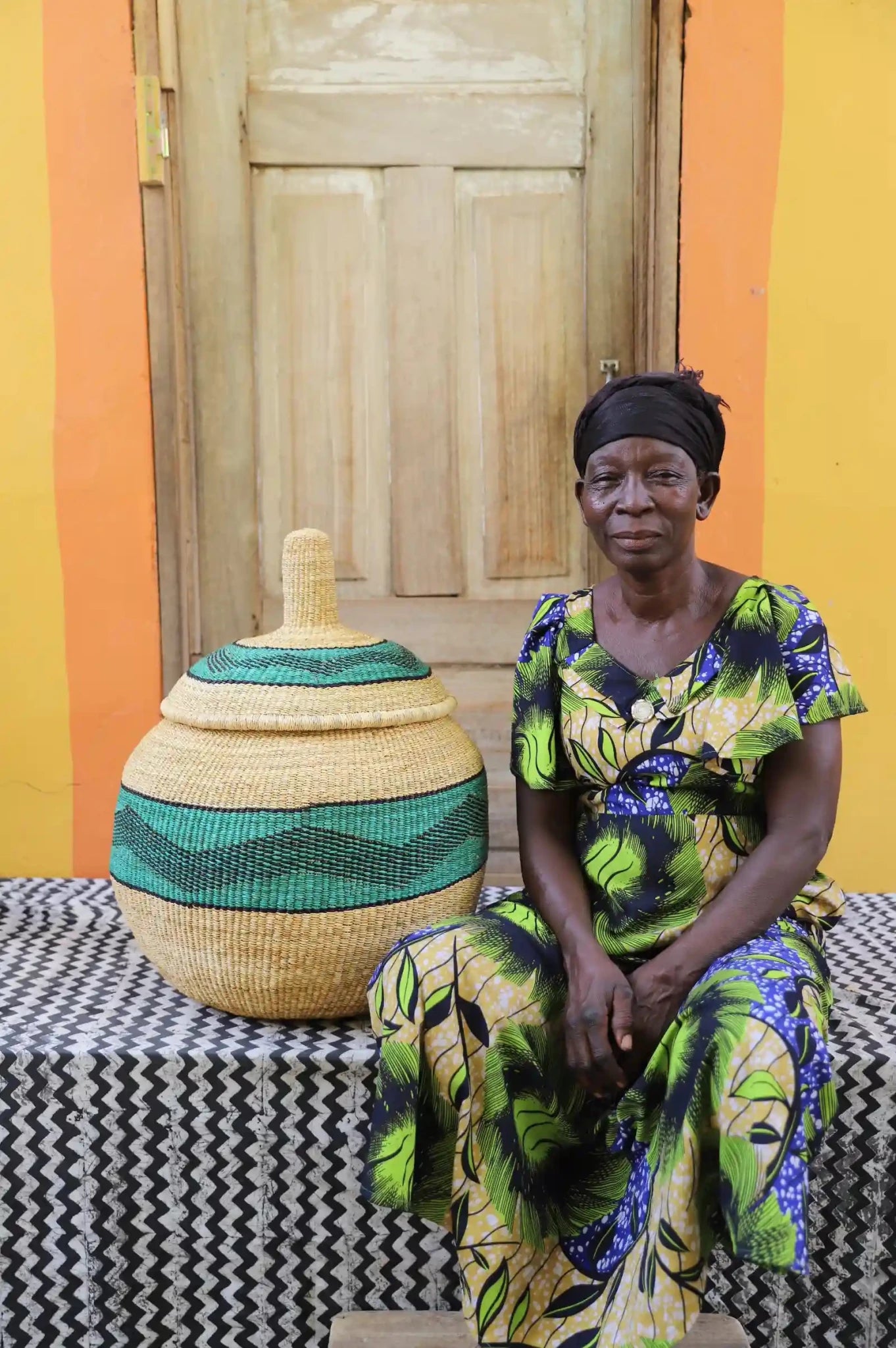 Woman seated beside large Orbit storage basket in natural straw with wide green stripe band