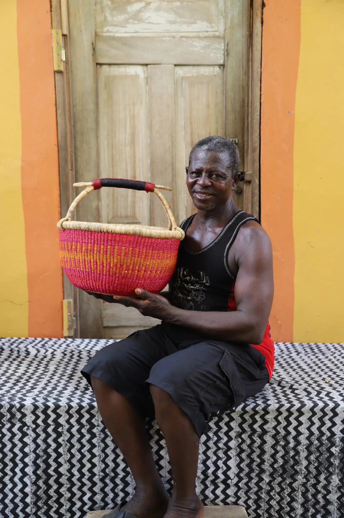 Man in black vest holding a vivid pink round Bolga shopping basket