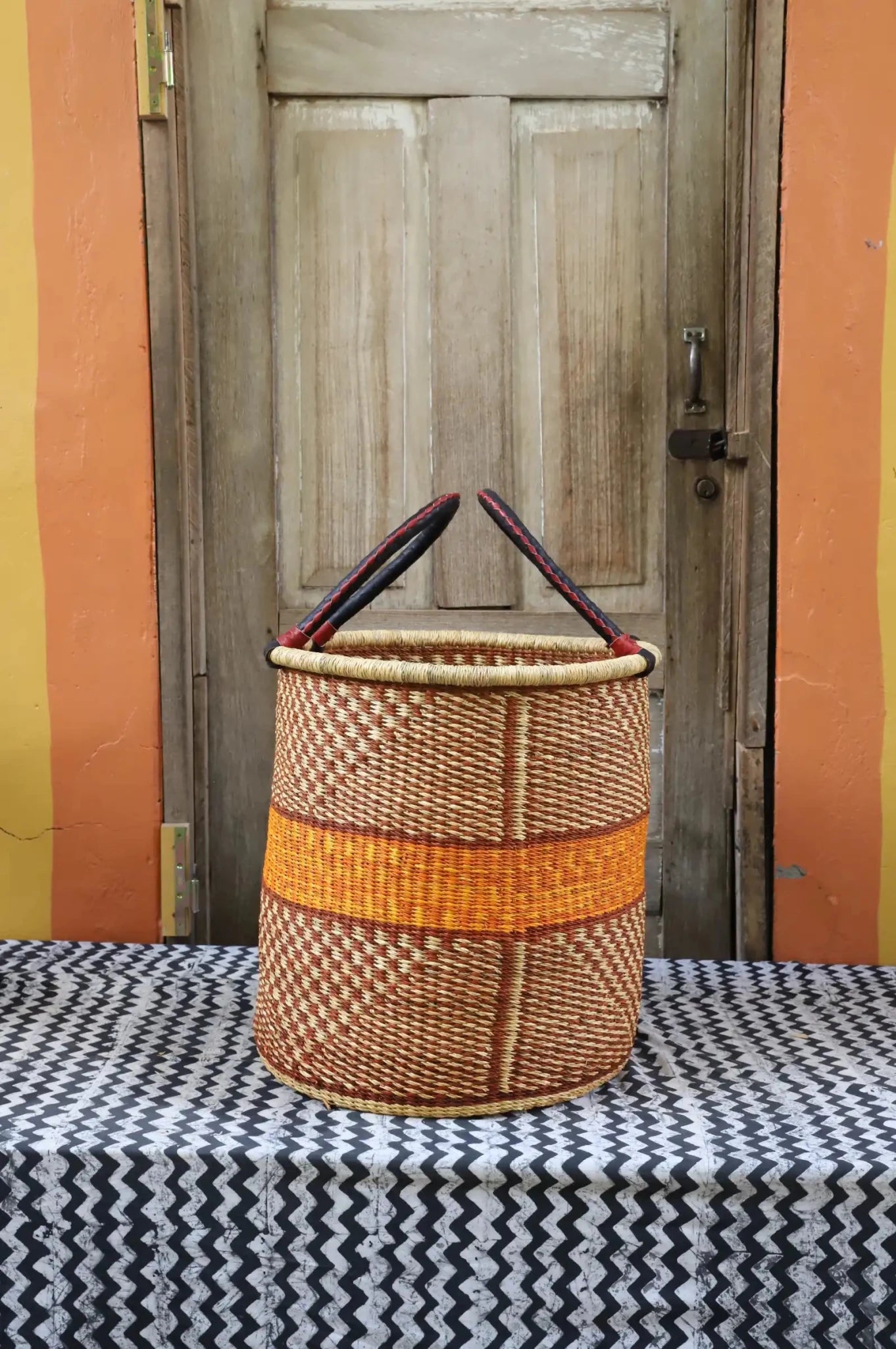 Colourful hand woven laundry basket sitting on black and white patterned cloth in front of a wooden door