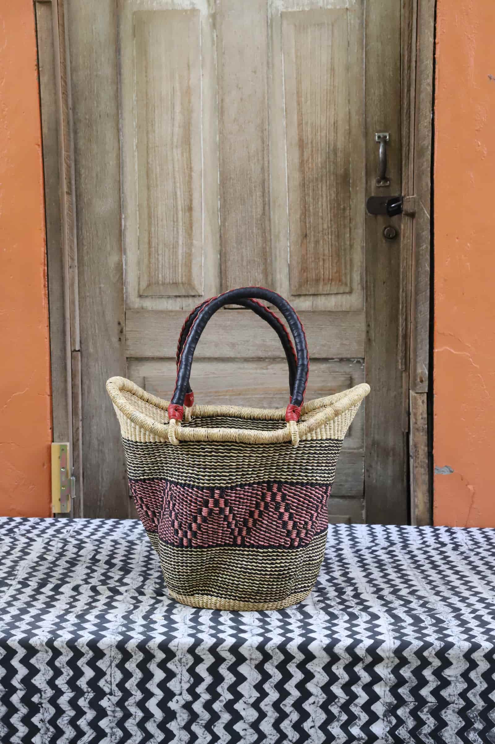 Woven carry on basket with premium leather on a black and white cloth against a wooden door