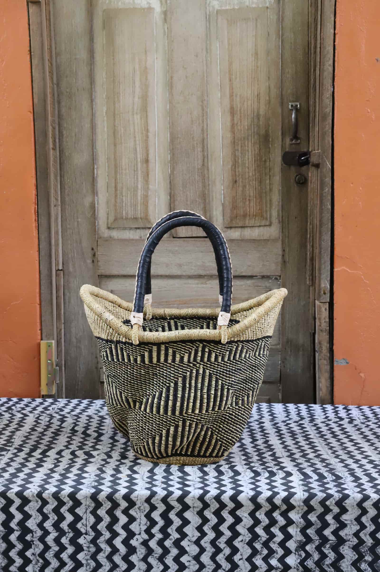 Woven carry on basket with premium leather on a black and white cloth against a wooden door