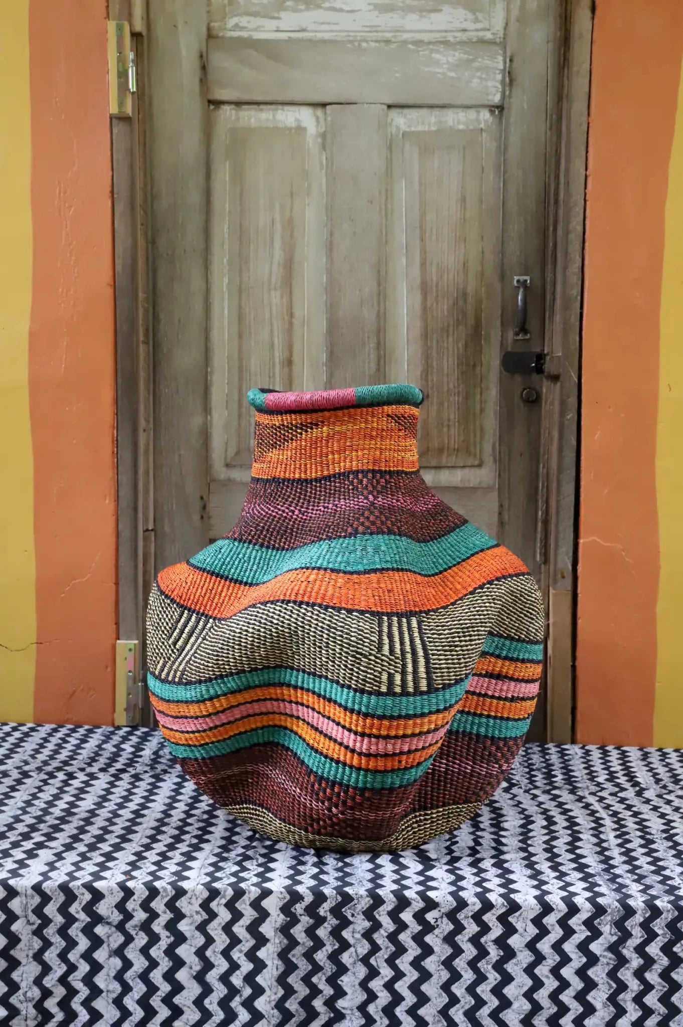 Colorful woven basket on a black and white patterned tablecloth with a wooden door in the background.