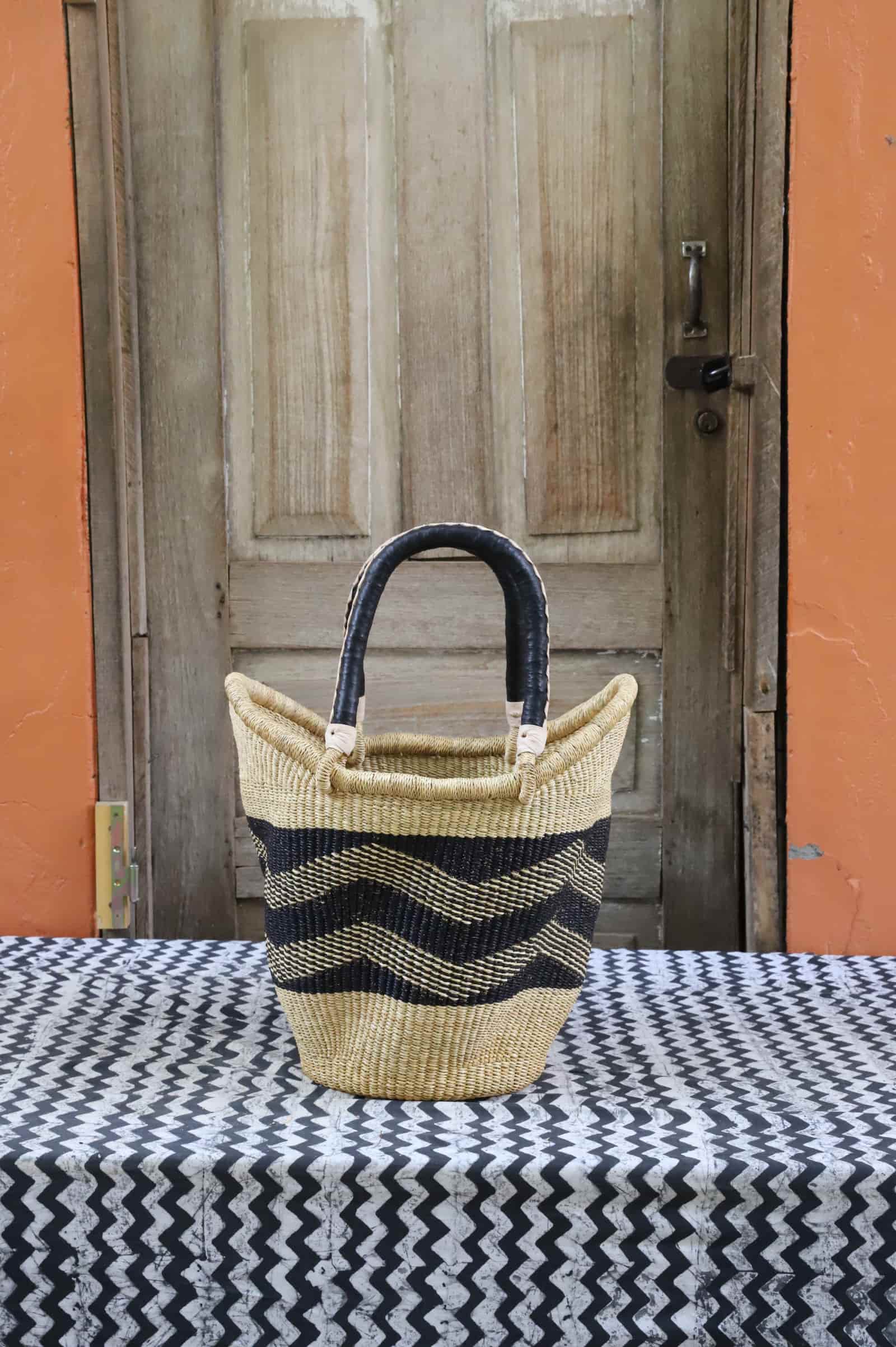 Woven carry on basket with premium leather on a black and white cloth against a wooden door