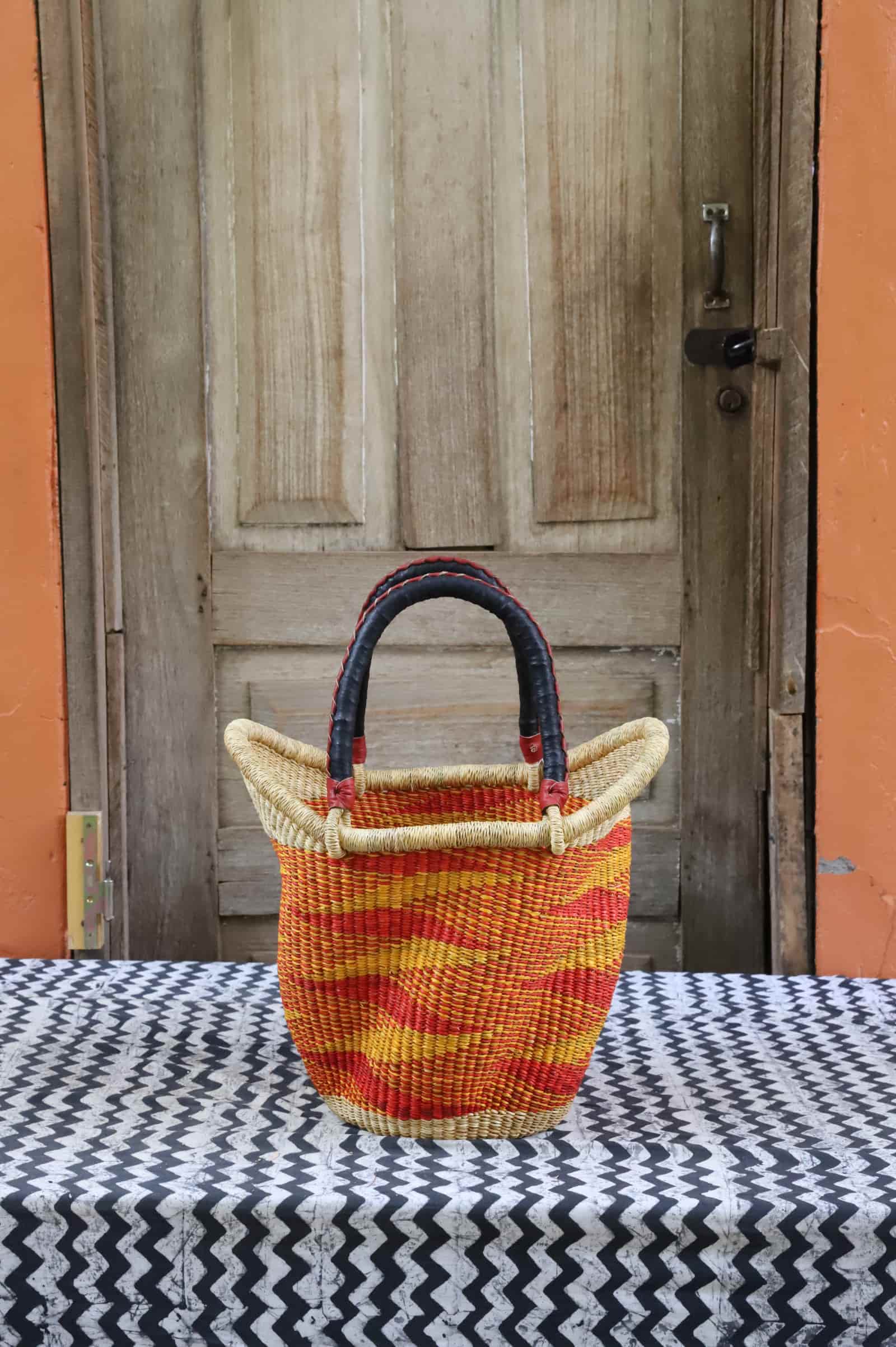 Woven carry on basket with premium leather on a black and white cloth against a wooden door