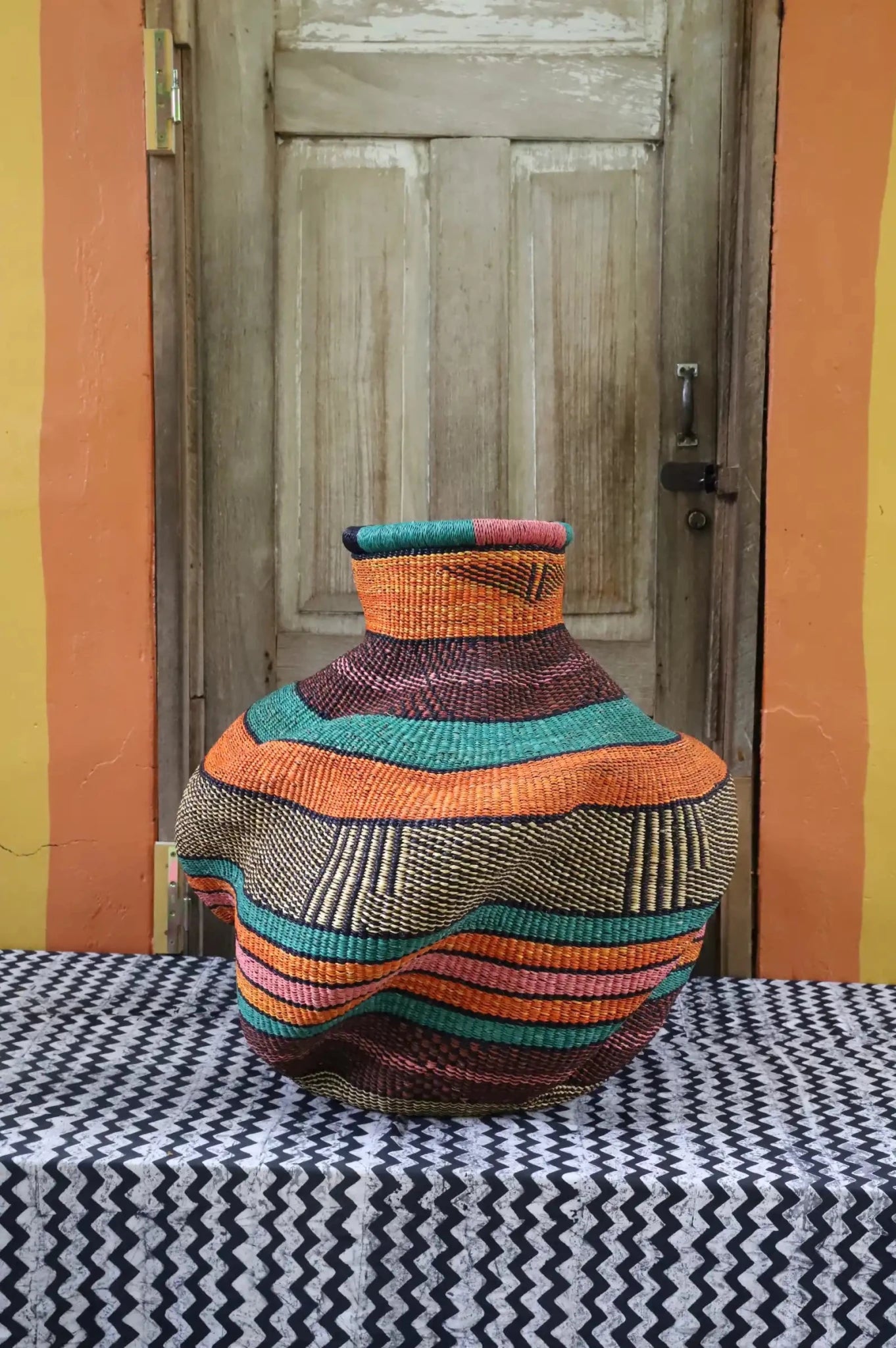Colorful woven basket on a table with a wooden door and an orange wall in the background
