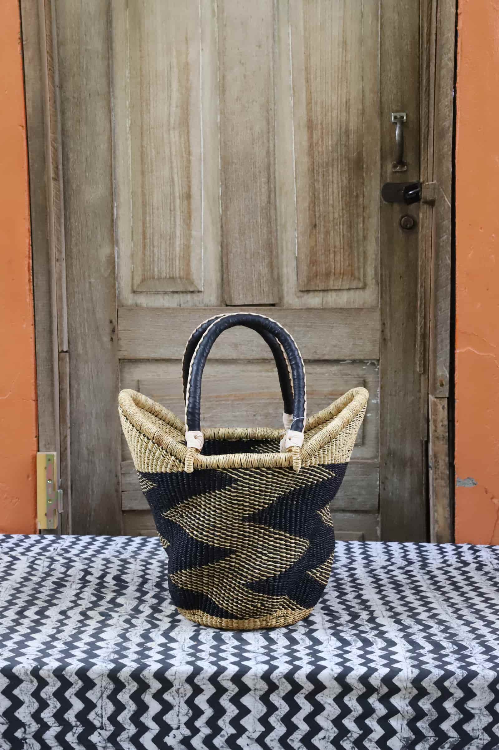 Woven carry on basket with premium leather on a black and white cloth against a wooden door