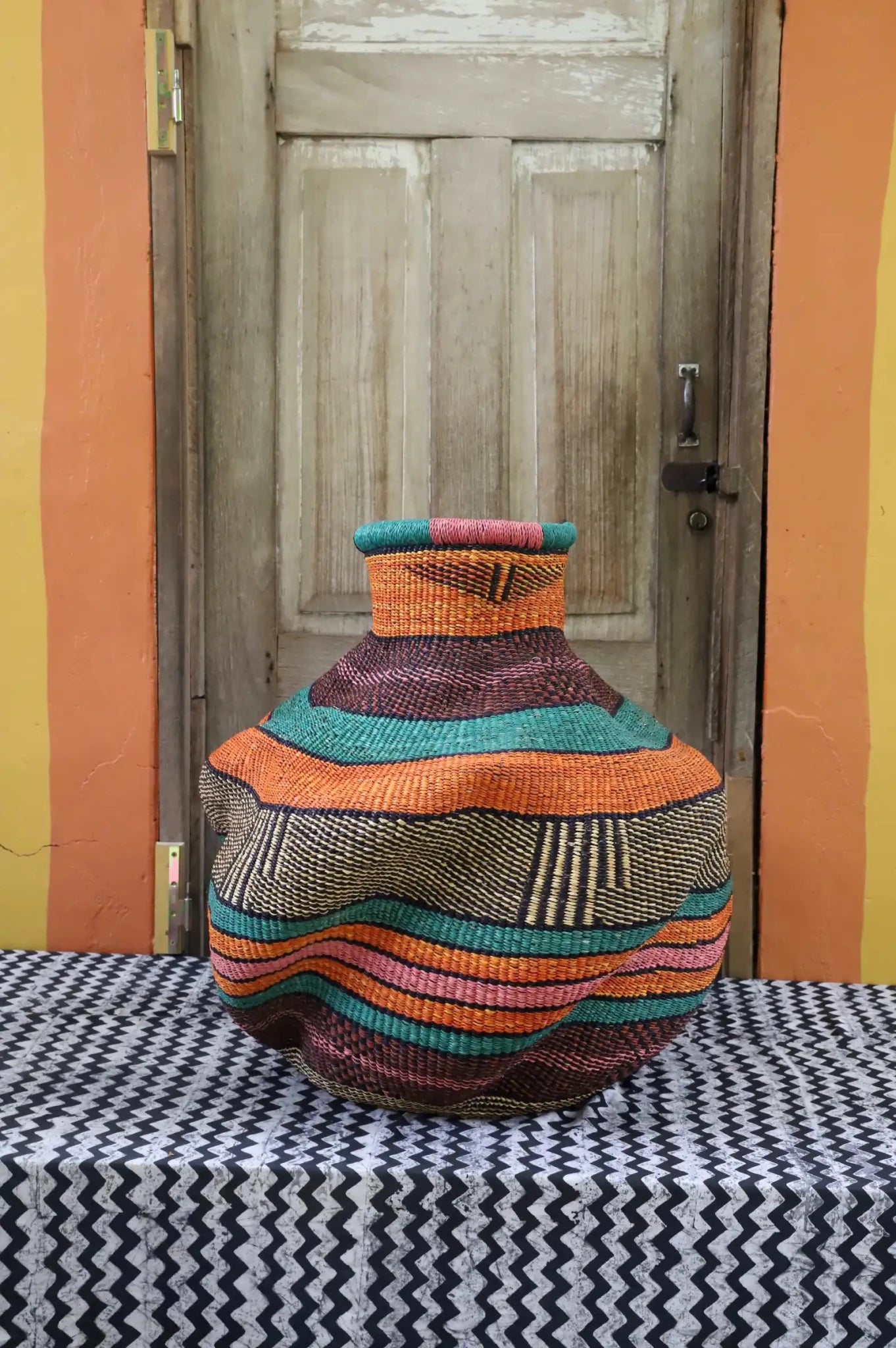 Colorful woven piece on a black and white patterned surface with a wooden door in the background.